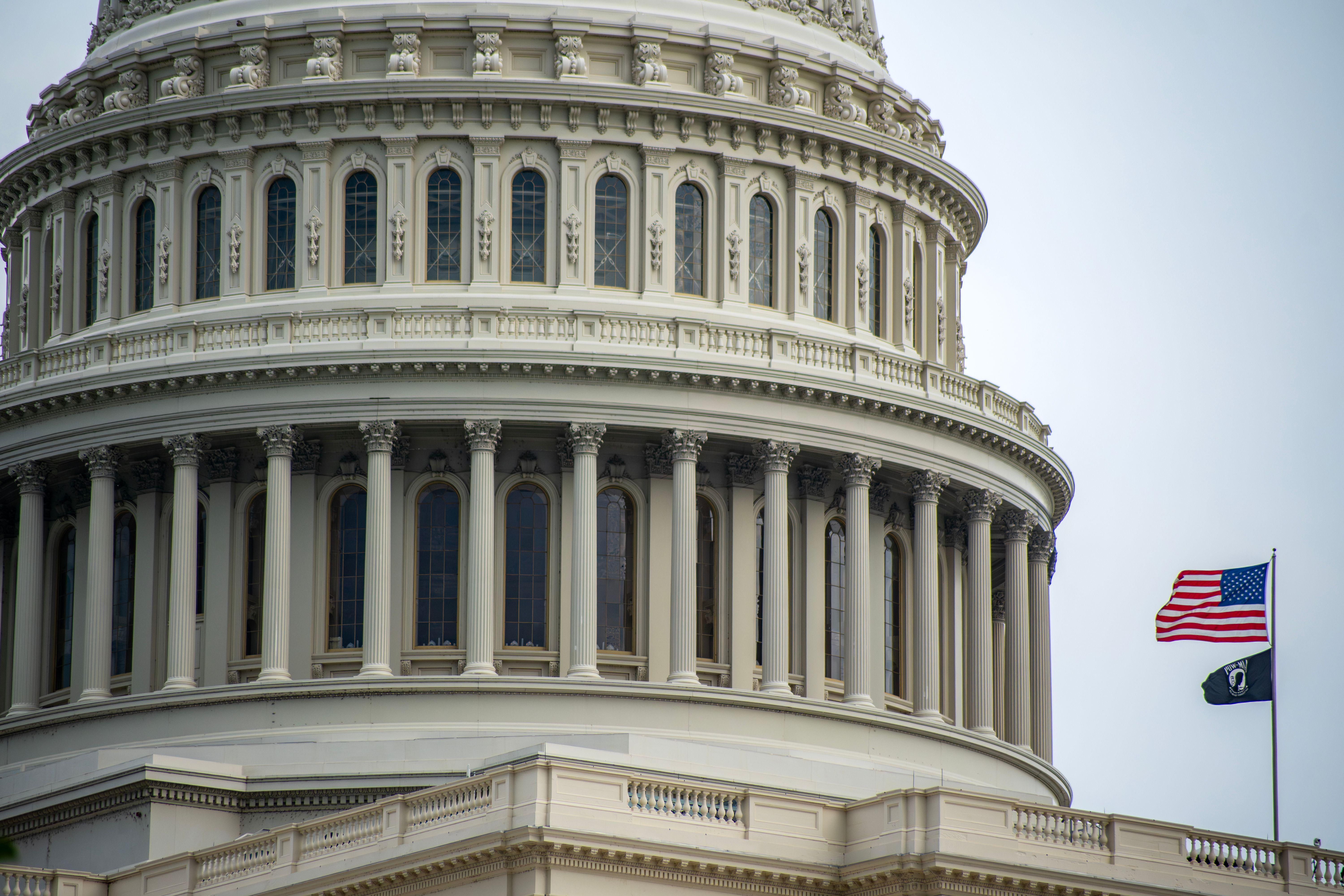 Detail of the US Capitol dome in Washington, D.C., featuring an American flag waving beside it.