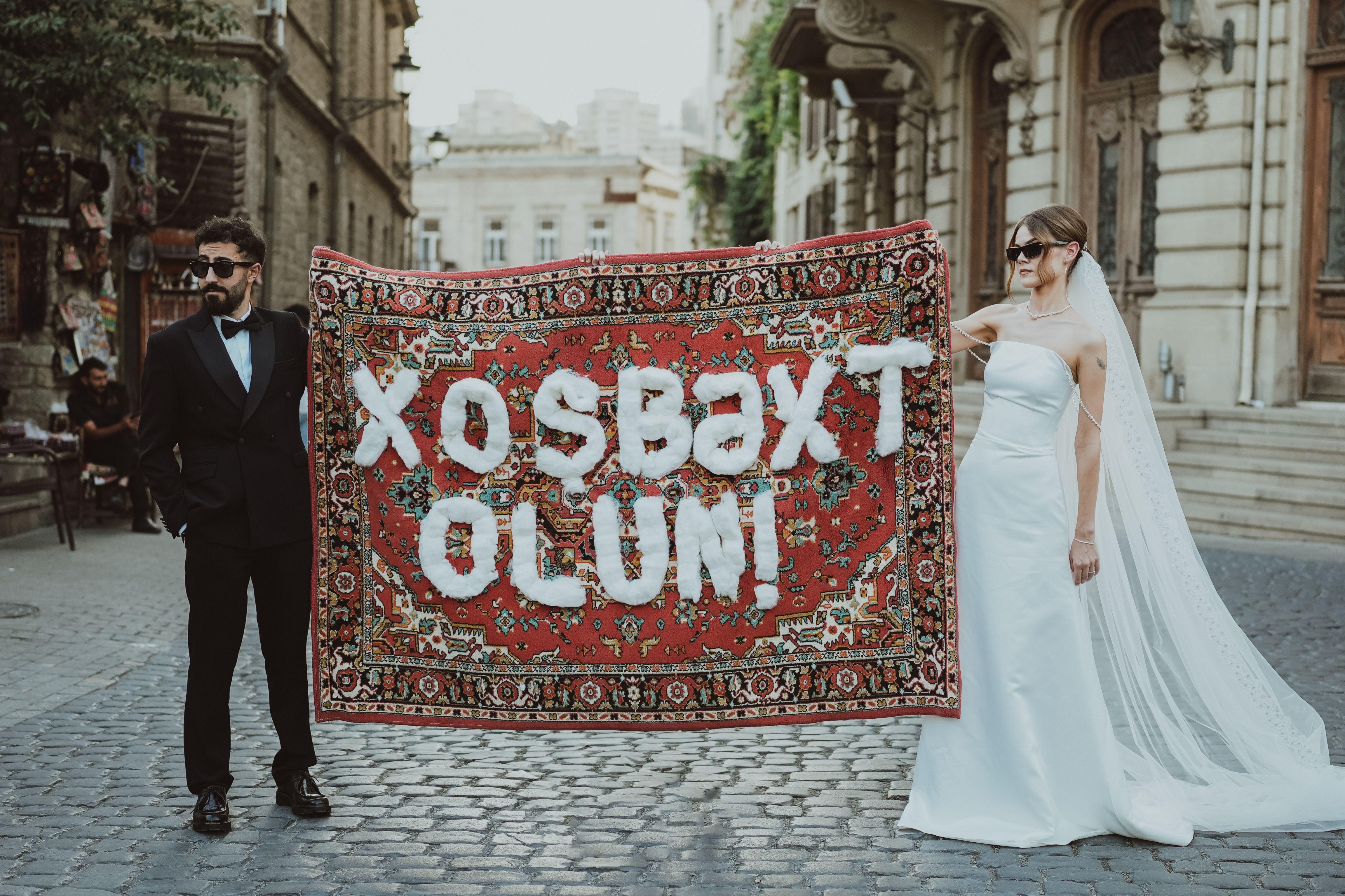 Stylish couple holds Azerbaijani carpet on cobbled street, embodying cultural elegance.