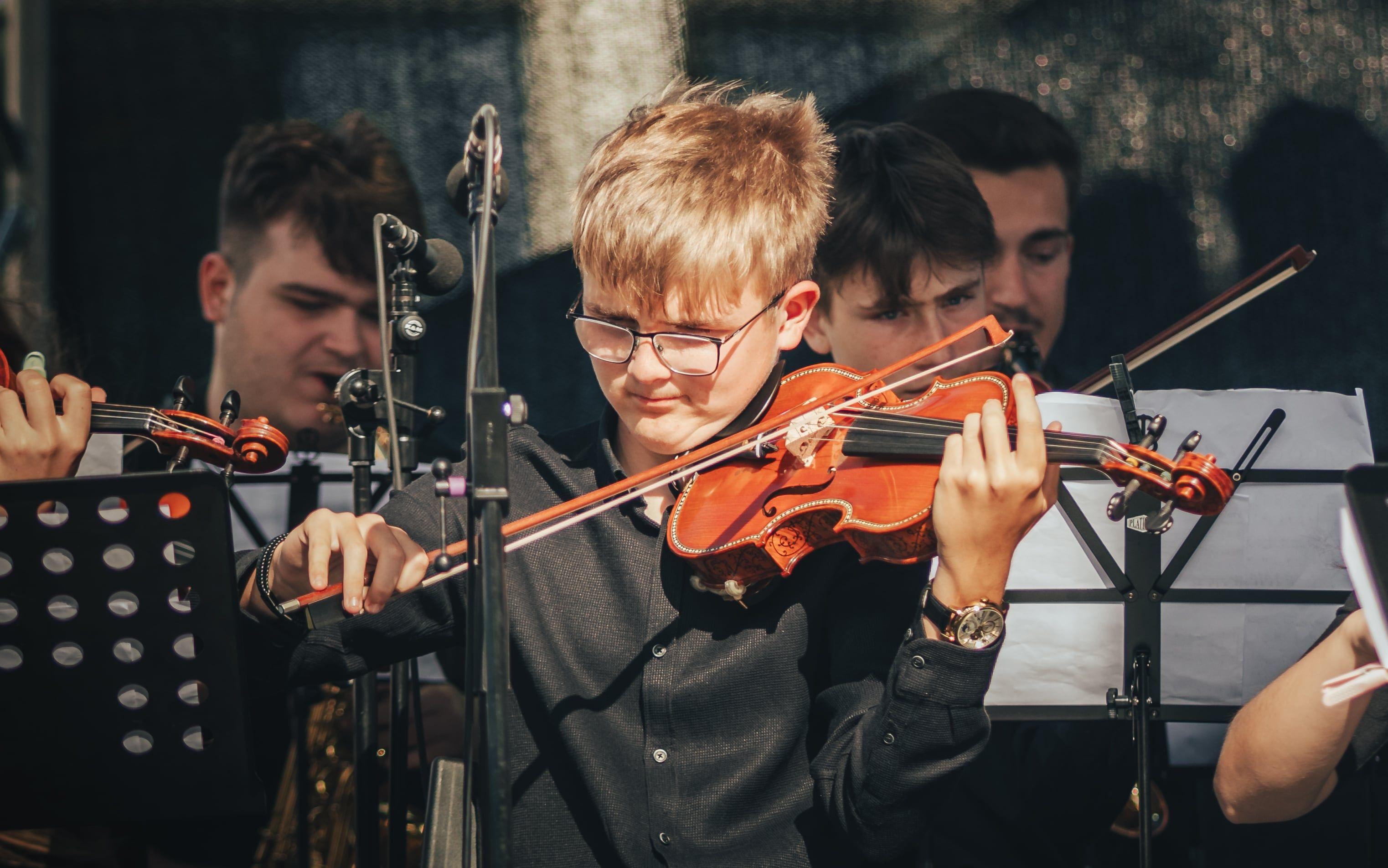 A young violinist passionately plays during an outdoor orchestra performance.