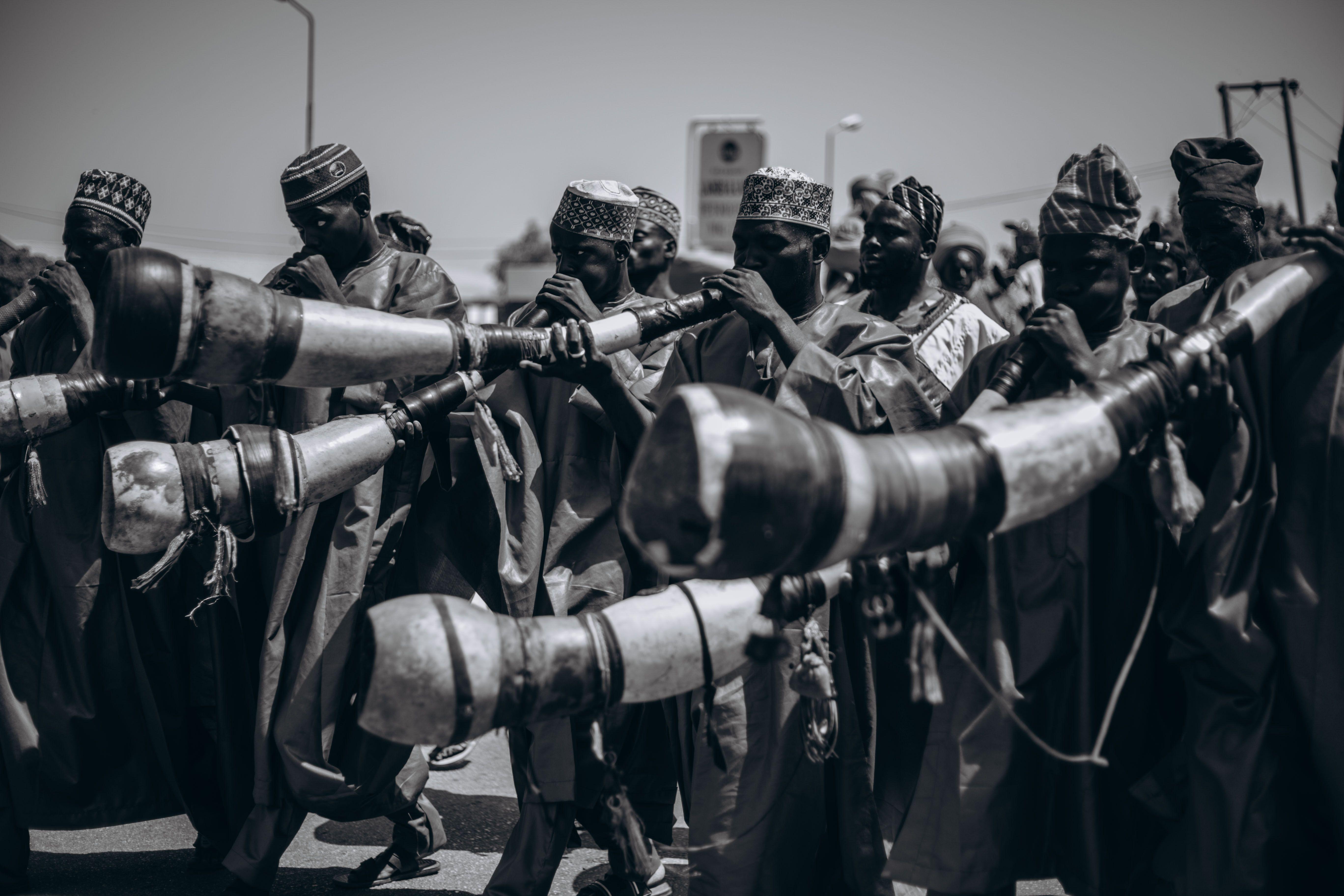 Black and white photo of African musicians playing traditional horns during a vibrant street parade.