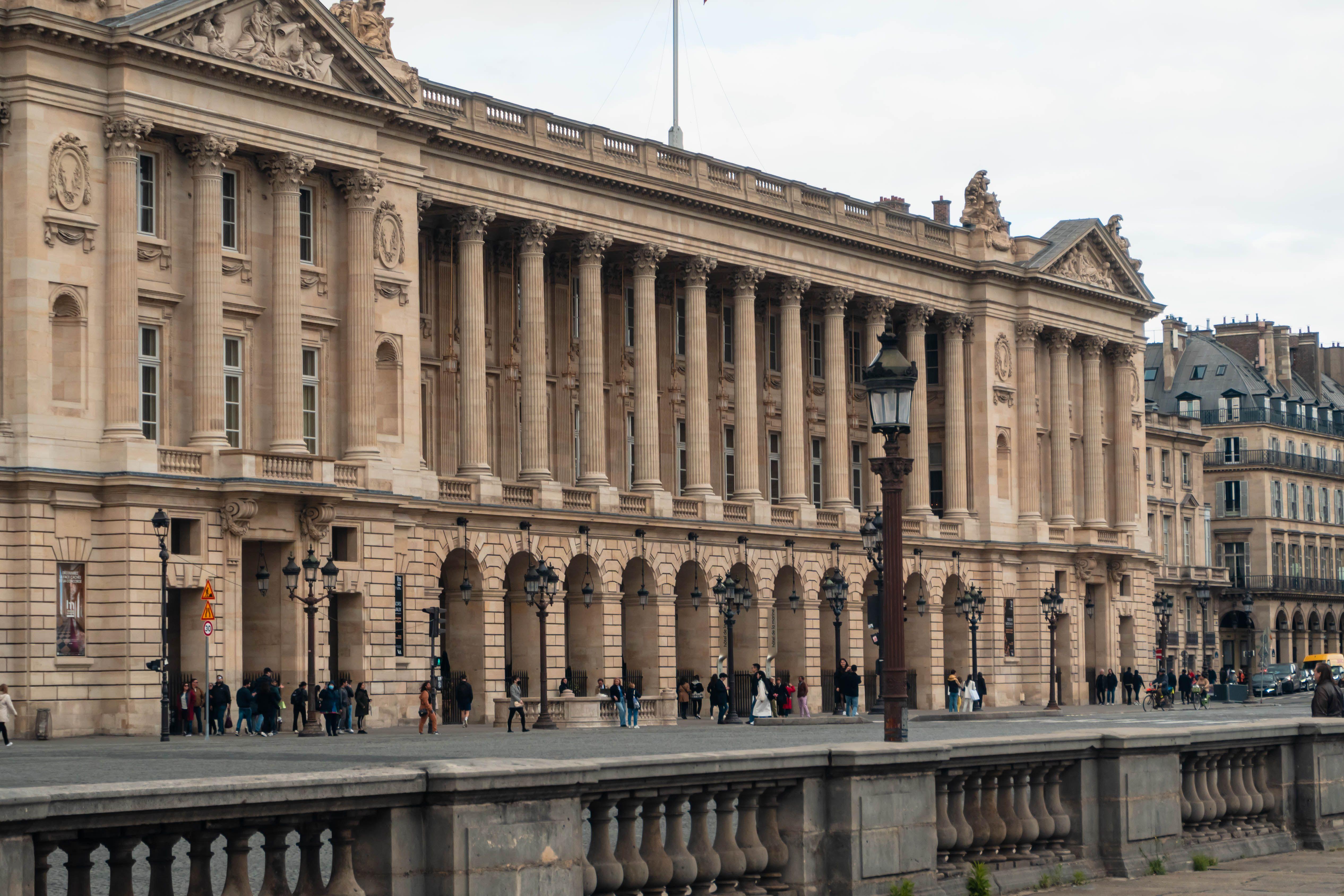 View of a neoclassical building facade in Paris with pedestrians walking below.