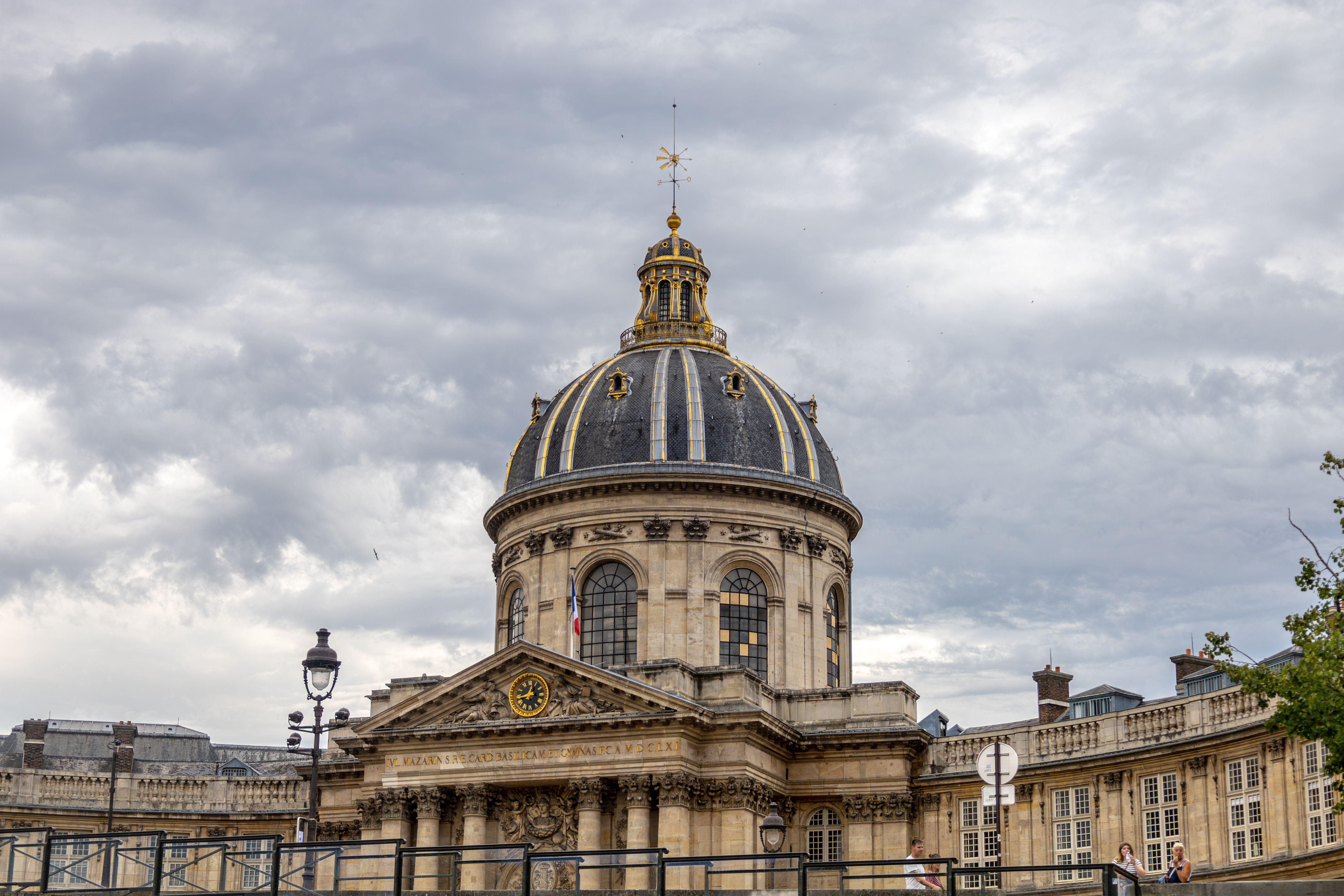 Architectural view of the iconic dome at the Institute of France in Paris under cloudy skies.
