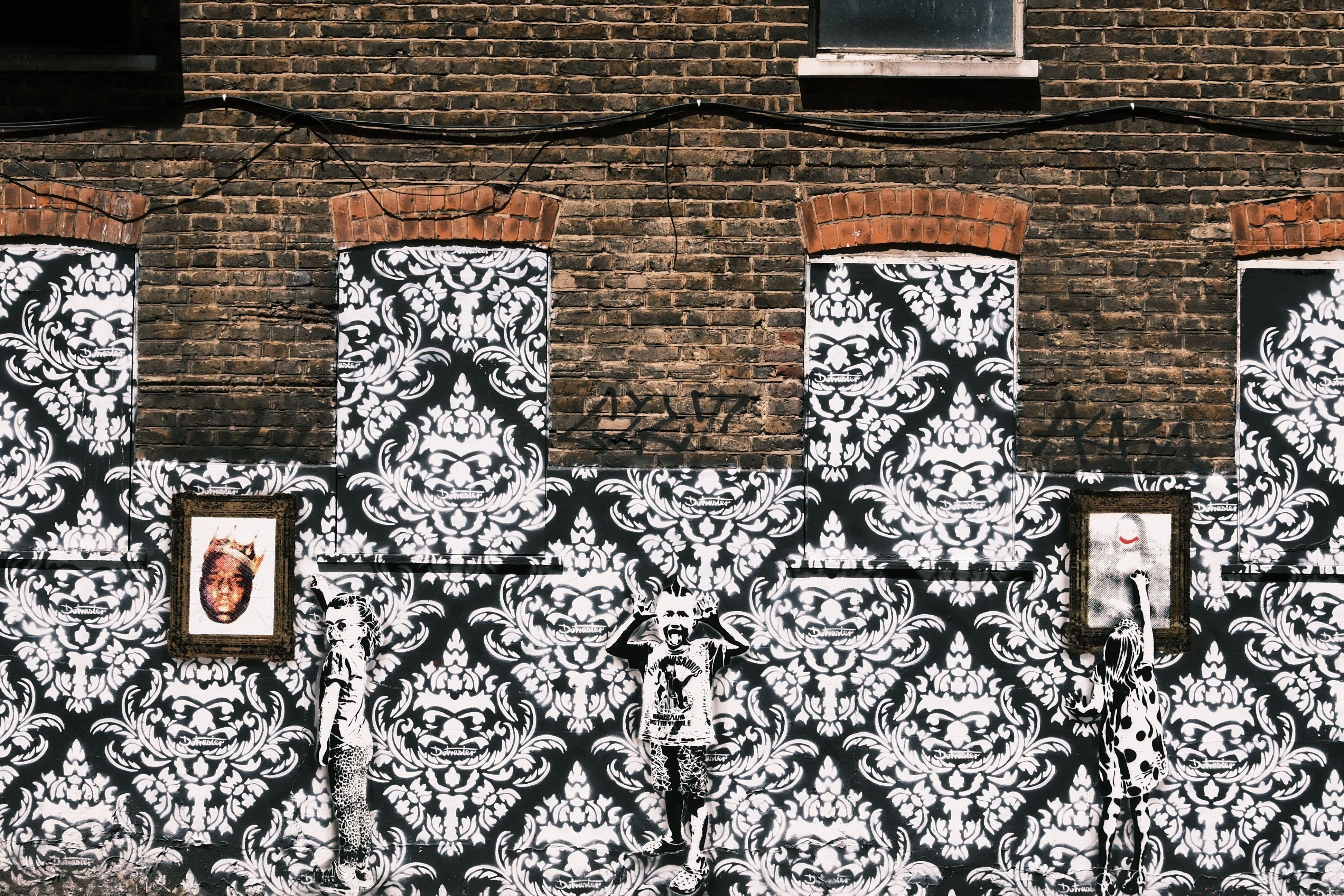 A richly textured street art mural with ornate patterns and framed portraits on a brick wall.
