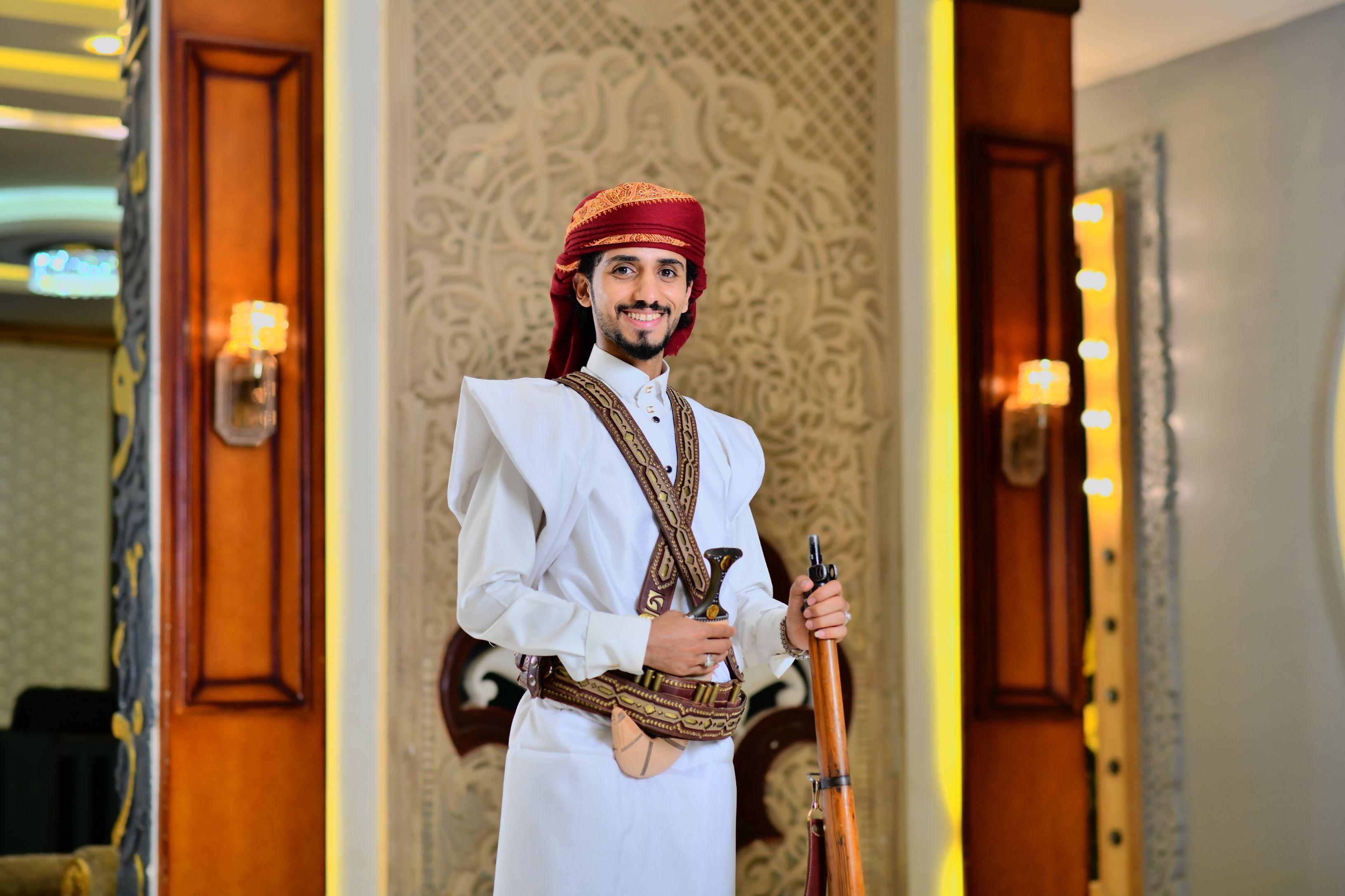Man in traditional Saudi Arabian attire with ornate decor in Makkah Province setting.