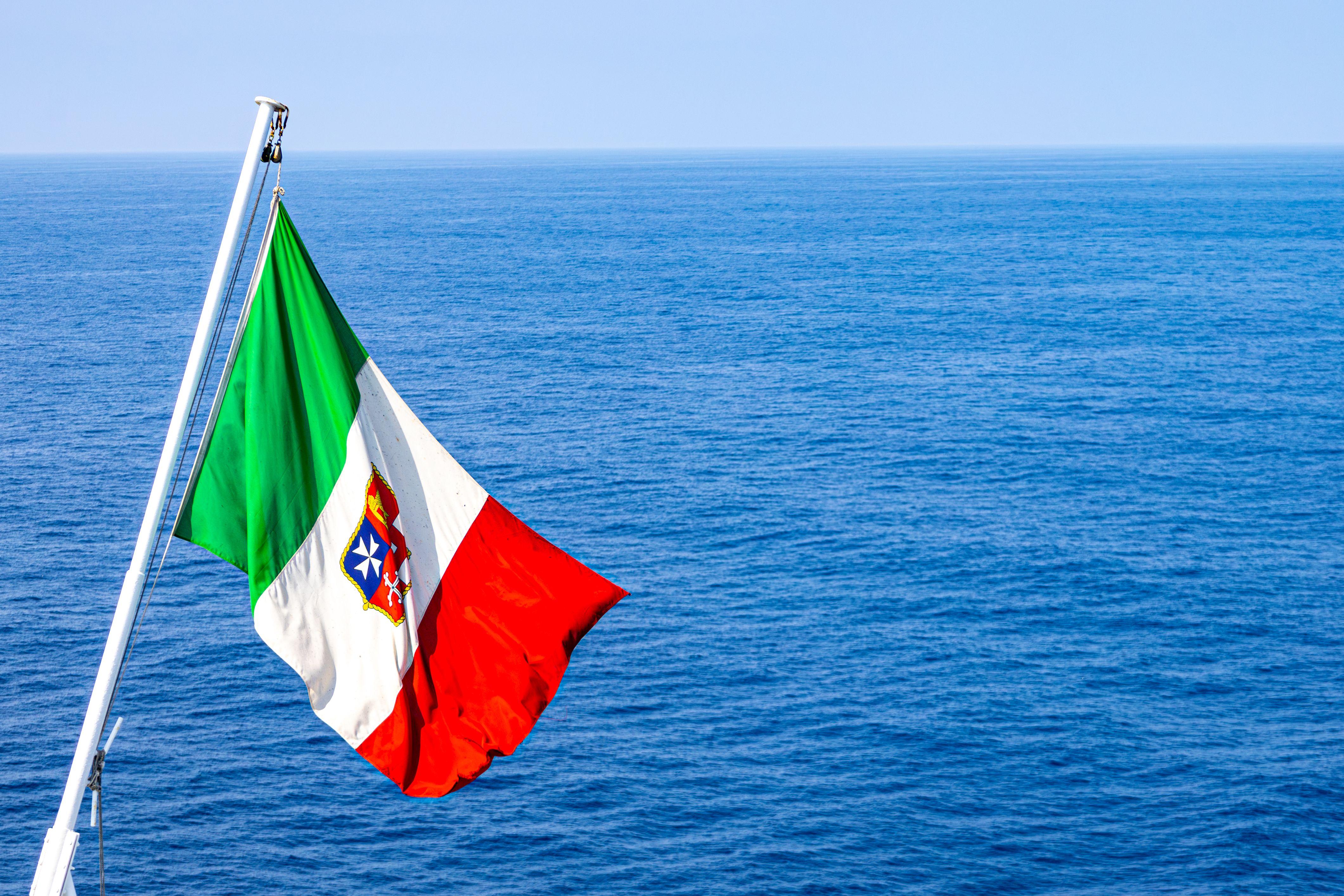 Colorful Italian maritime flag waving against the expansive blue Mediterranean Sea near Barcelona.