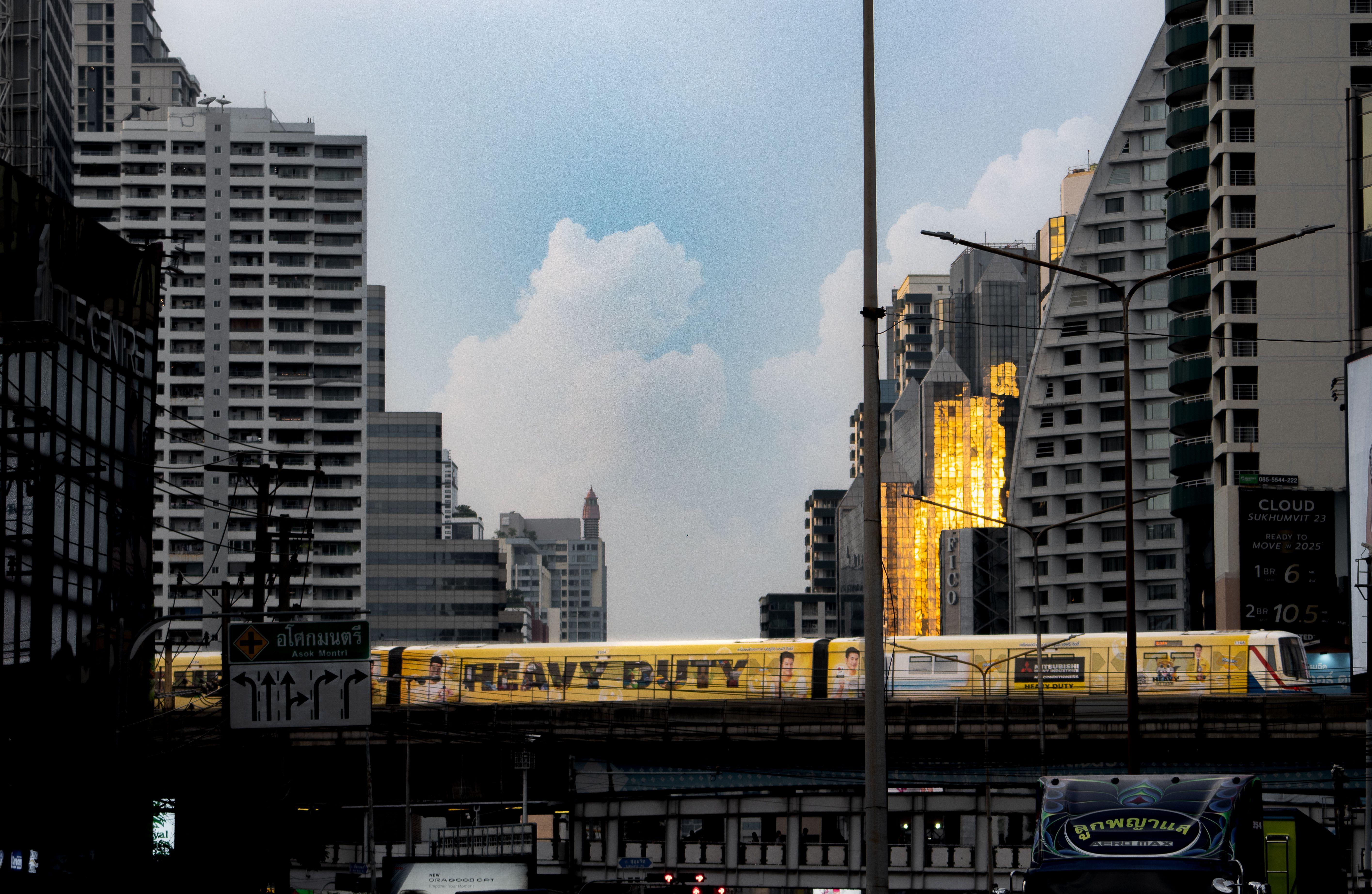 Cityscape featuring Bangkok's skytrain with golden reflections on skyscrapers at sunset.