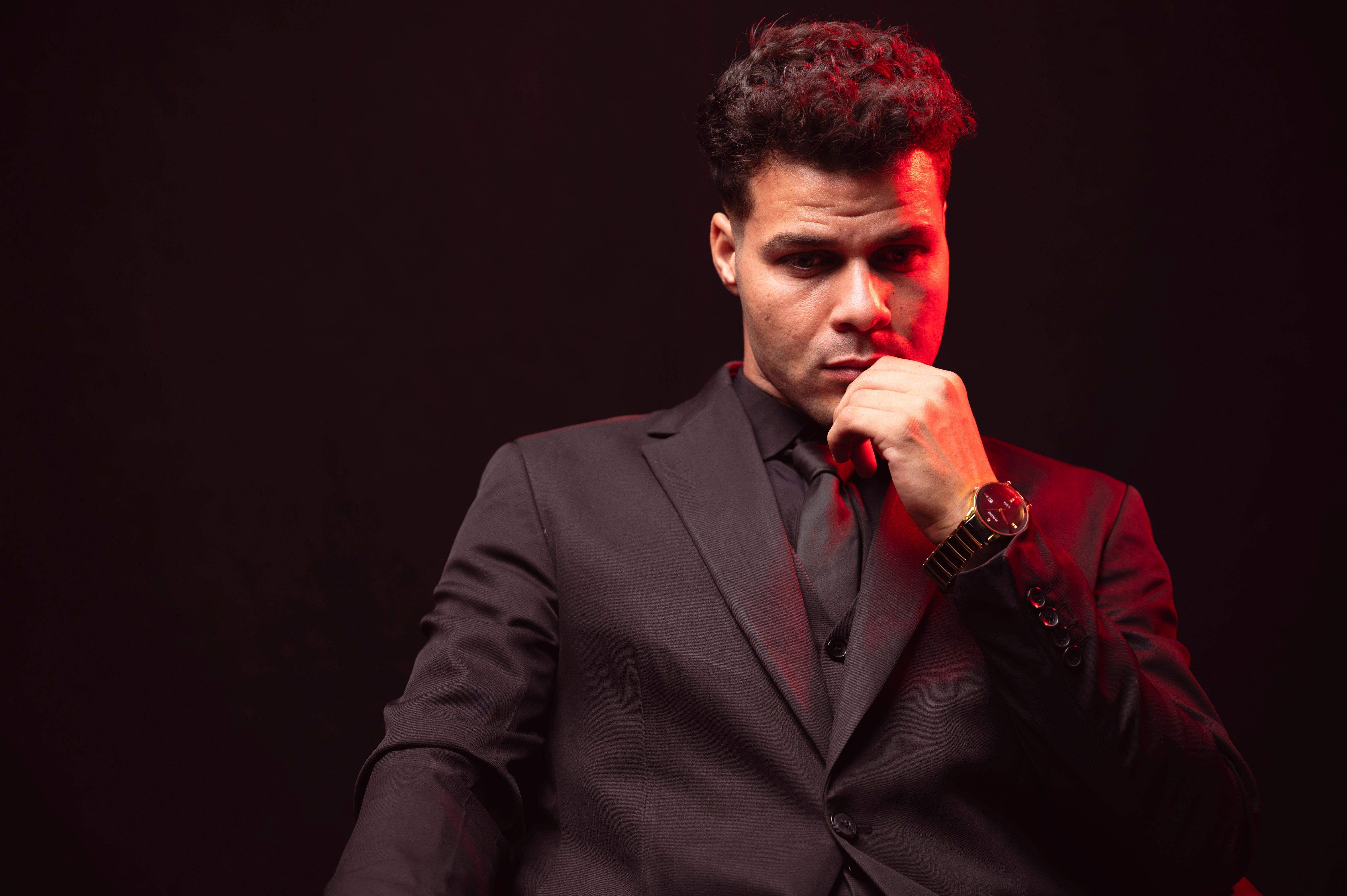 Portrait of a thoughtful man in a black suit with a red light accent in a moody setting.