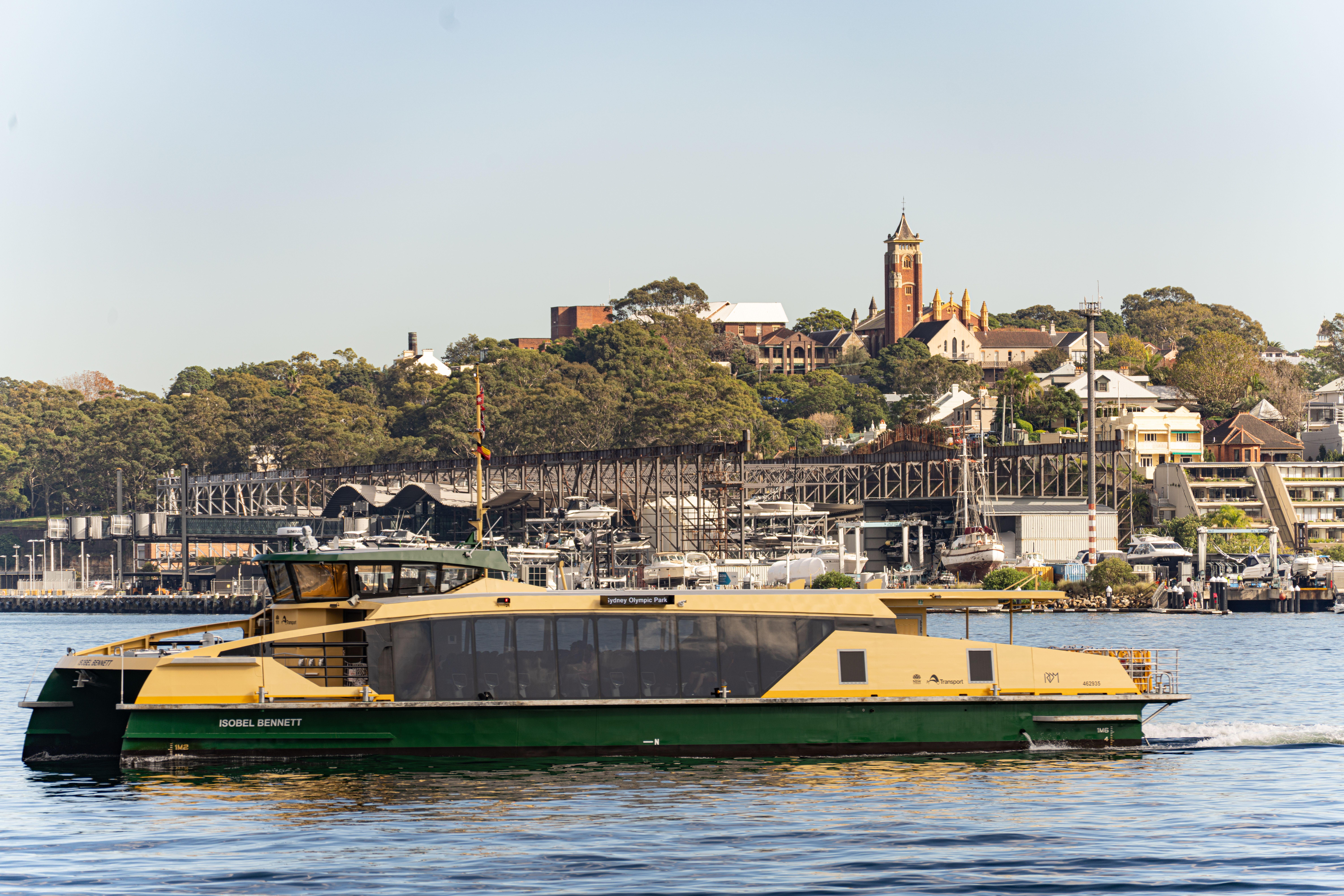 A ferry glides by Barangaroo with cityscape and lush greenery in the background.