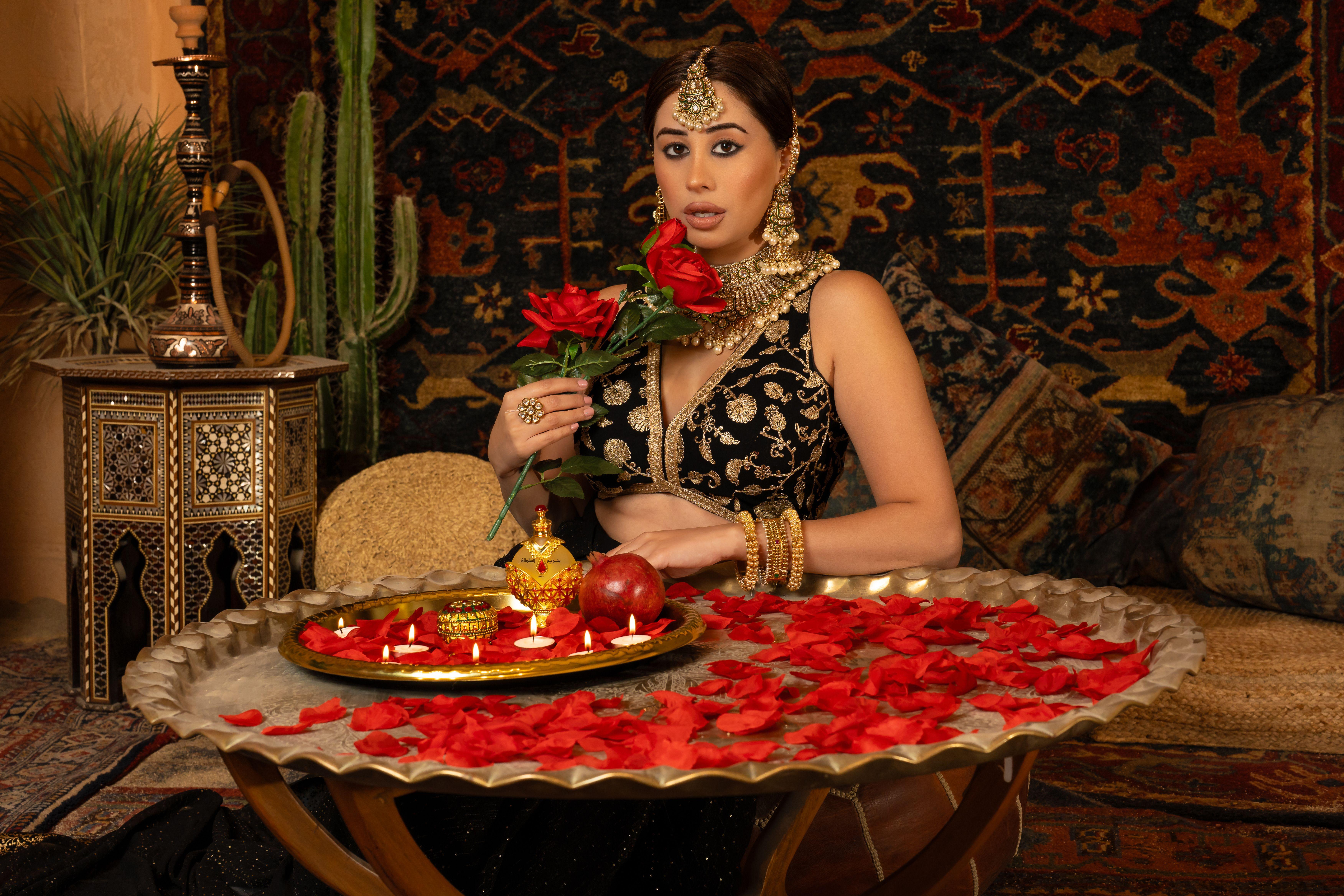 A woman in traditional attire holding roses, surrounded by lavish decor and jewelry.