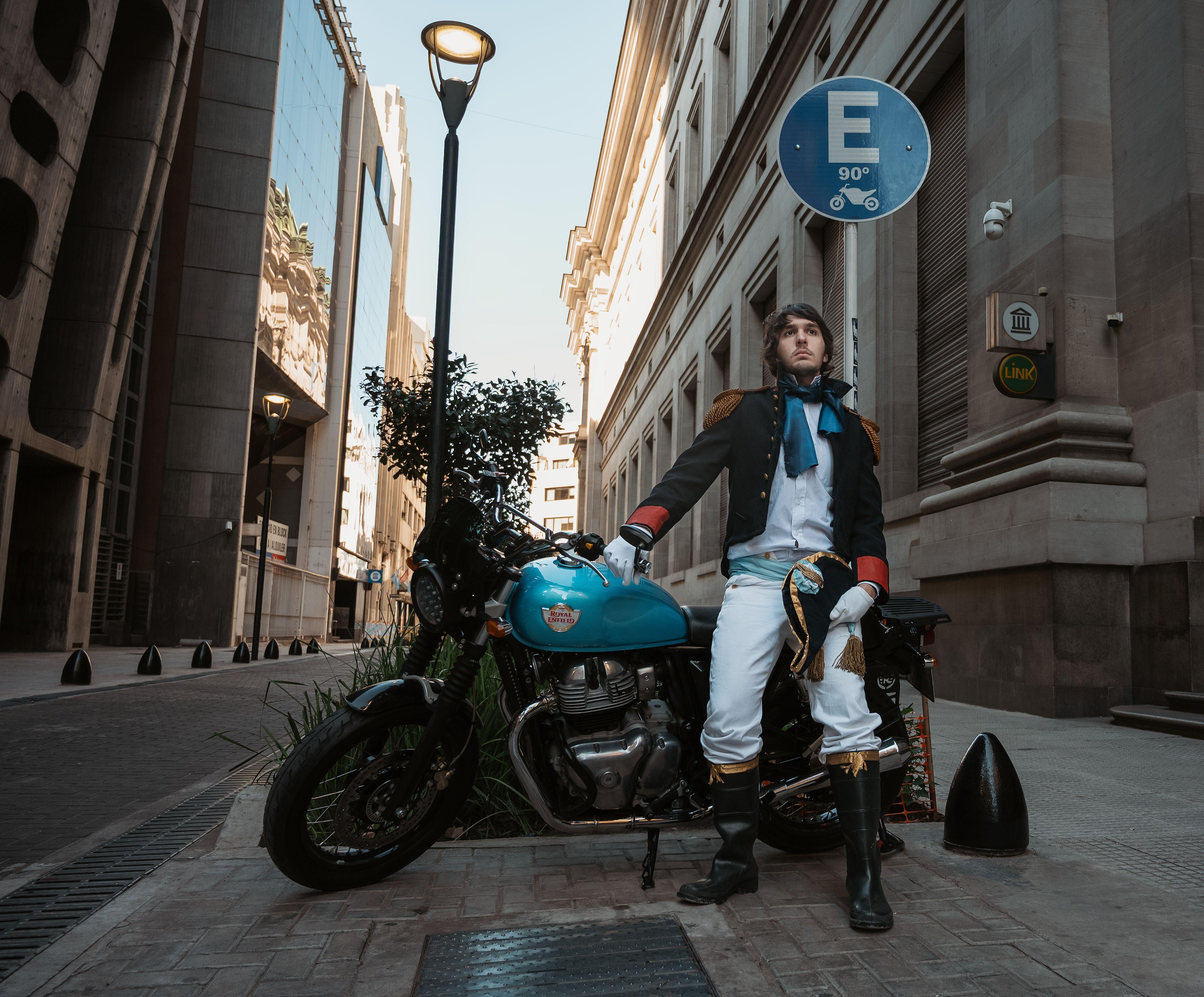 Young man in a historical costume poses with a motorcycle on a street in Buenos Aires.