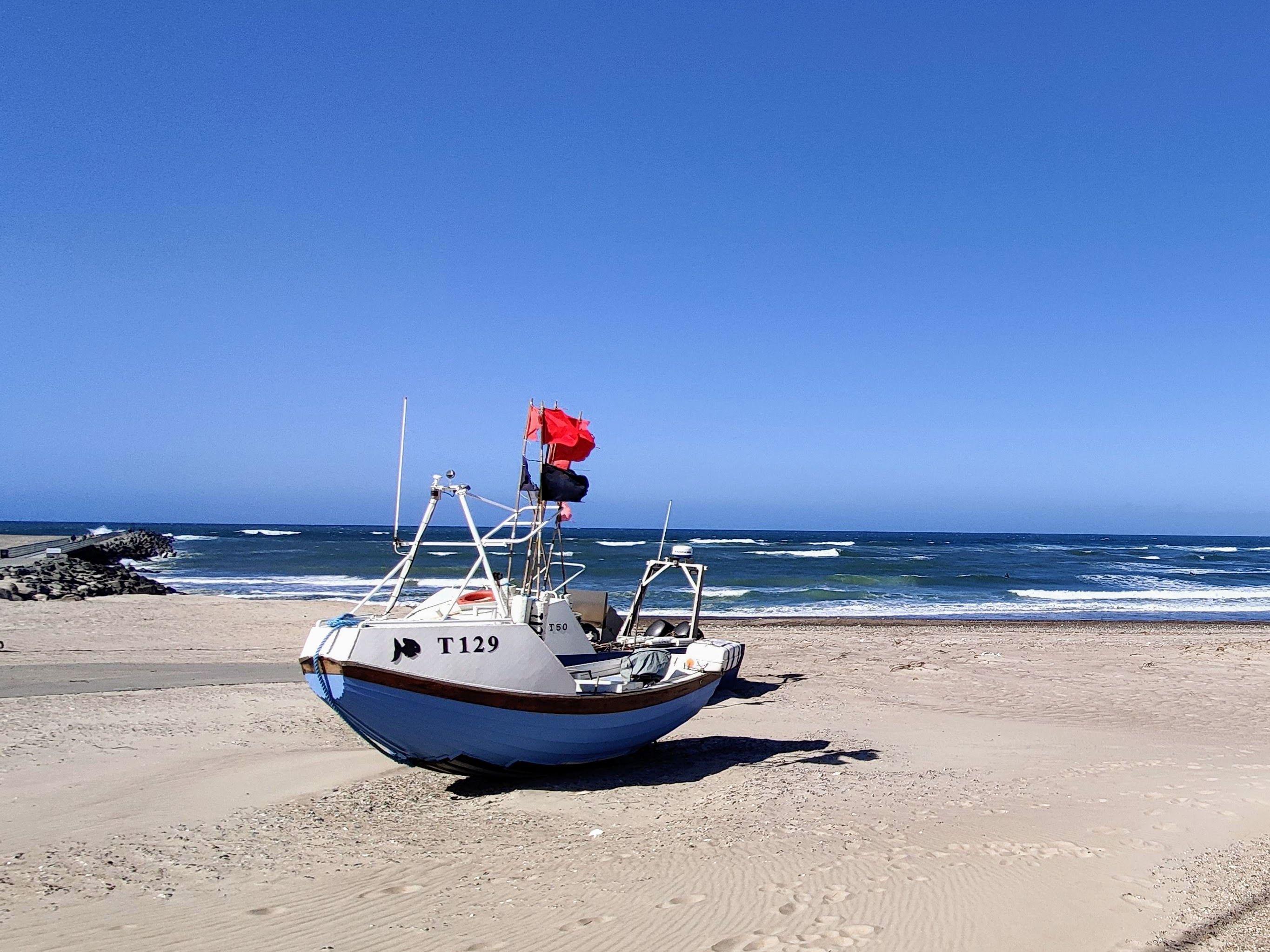 Fishing boat on a sandy beach under a clear blue sky, showcasing the calm sea and coastline.