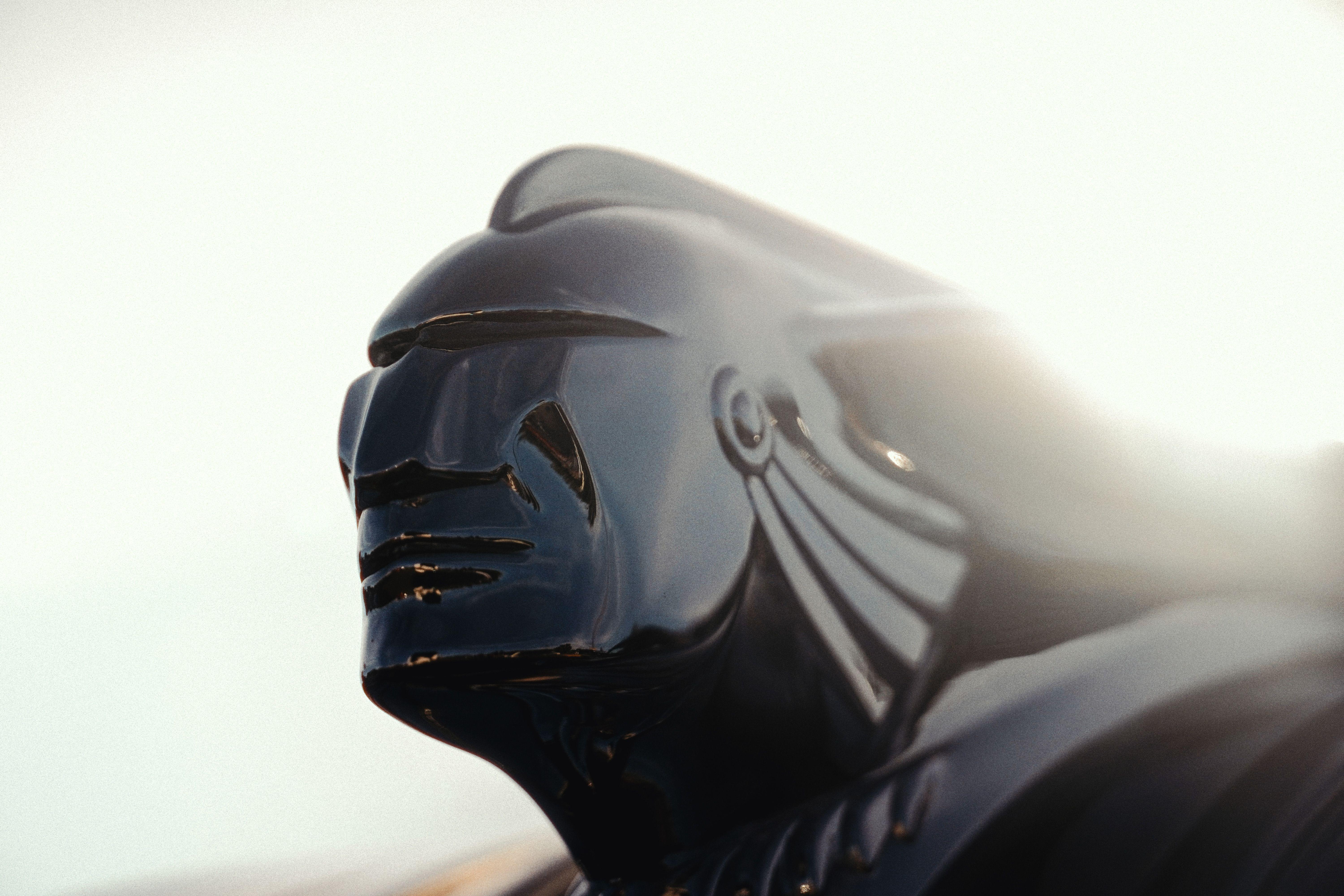 Dramatic close-up of a vintage car hood ornament, highlighting its intricate design under bright light.