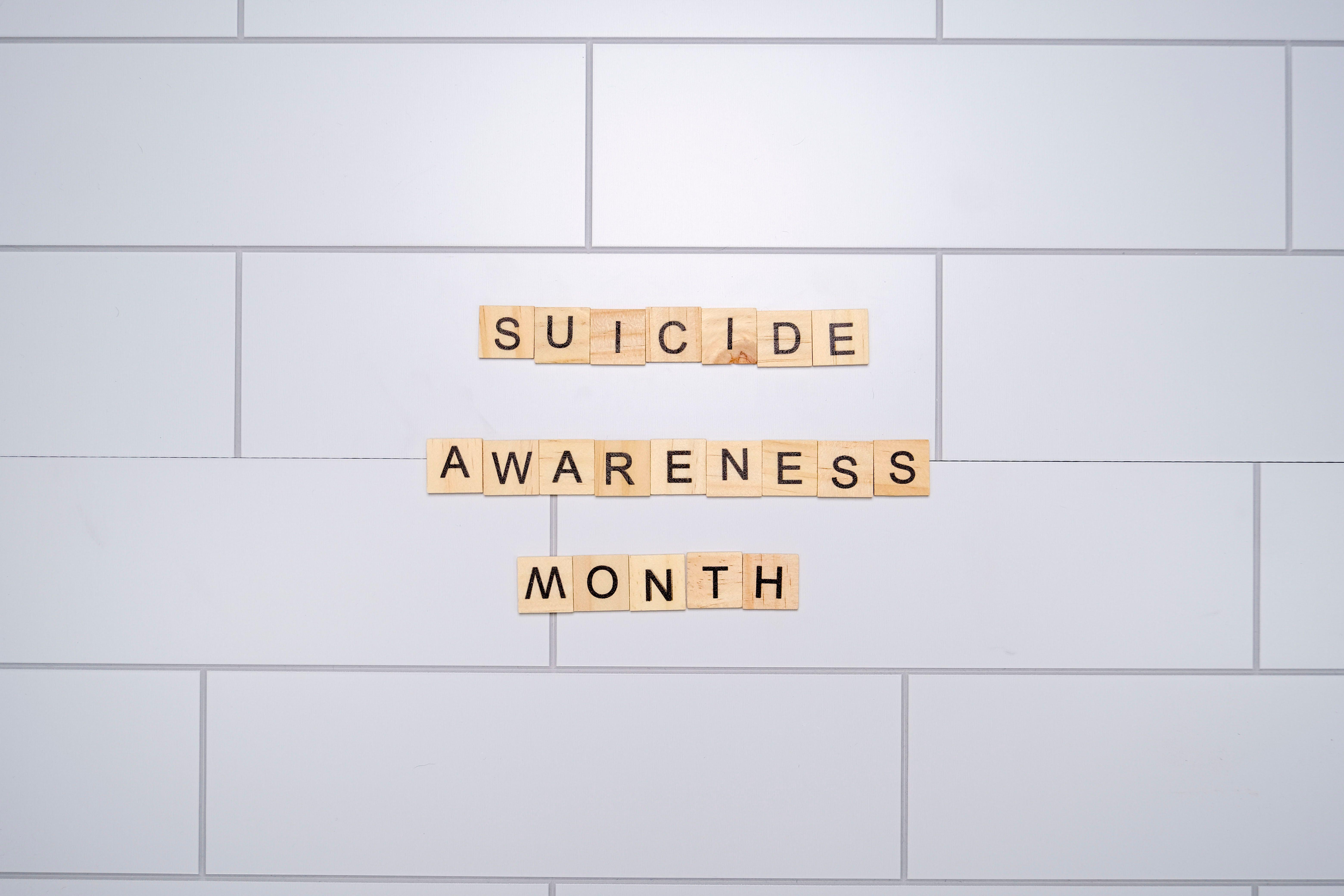 Suicide Awareness Month spelled with Scrabble tiles on a light background symbolizes mental health awareness.