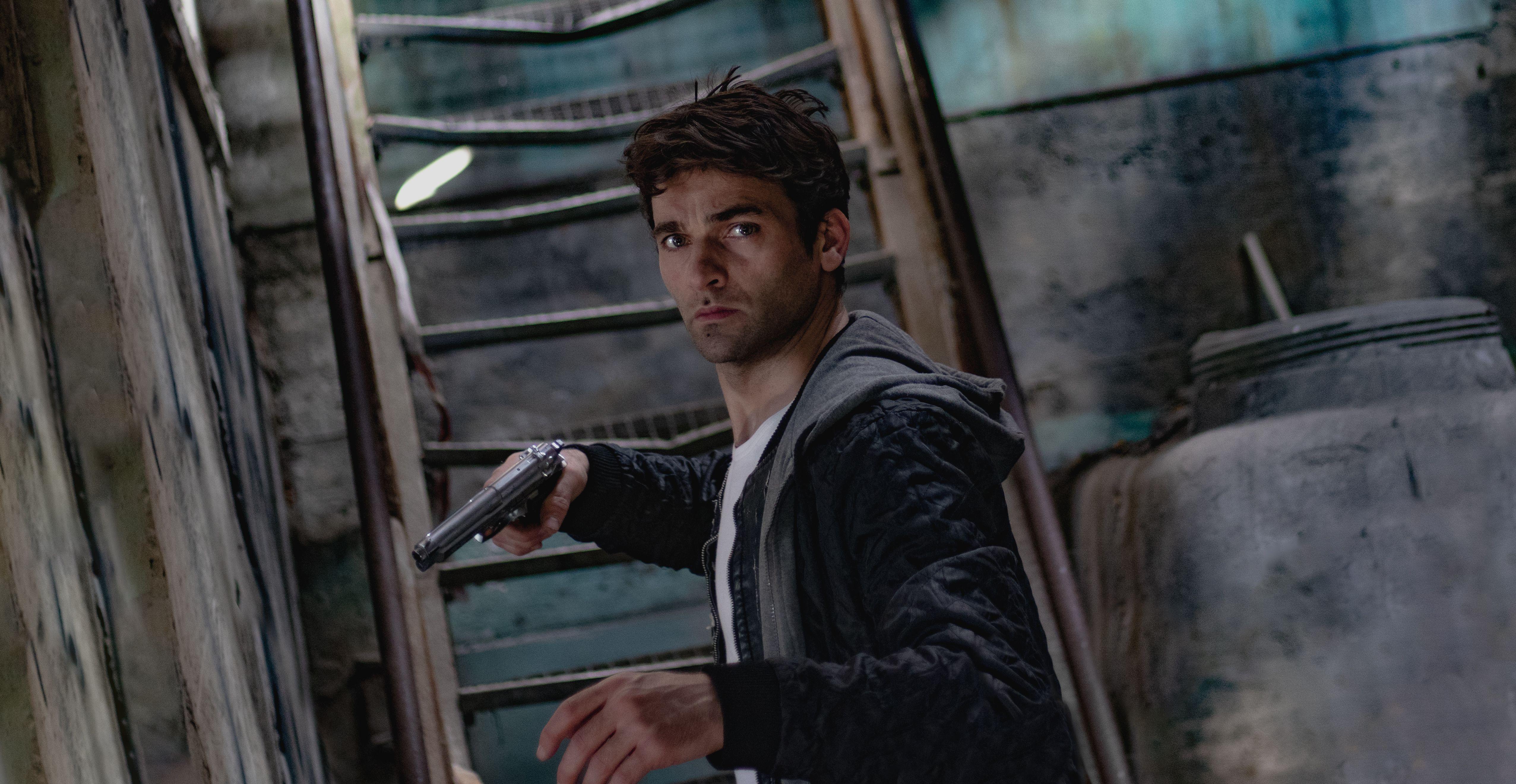 A man holding a gun in a dimly lit, mysterious urban setting.