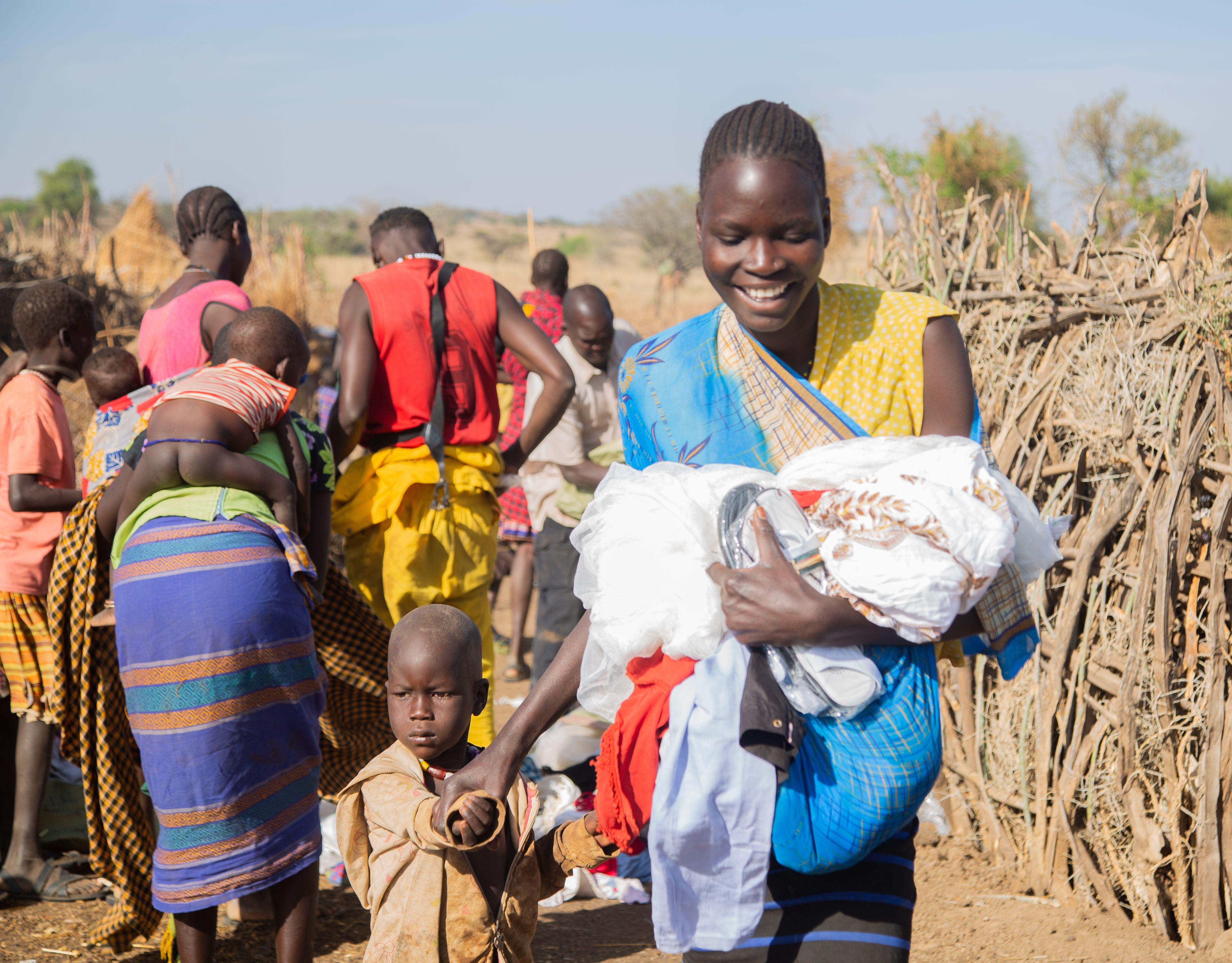 A joyful African woman carries a child in a vibrant village setting, highlighting community spirit.