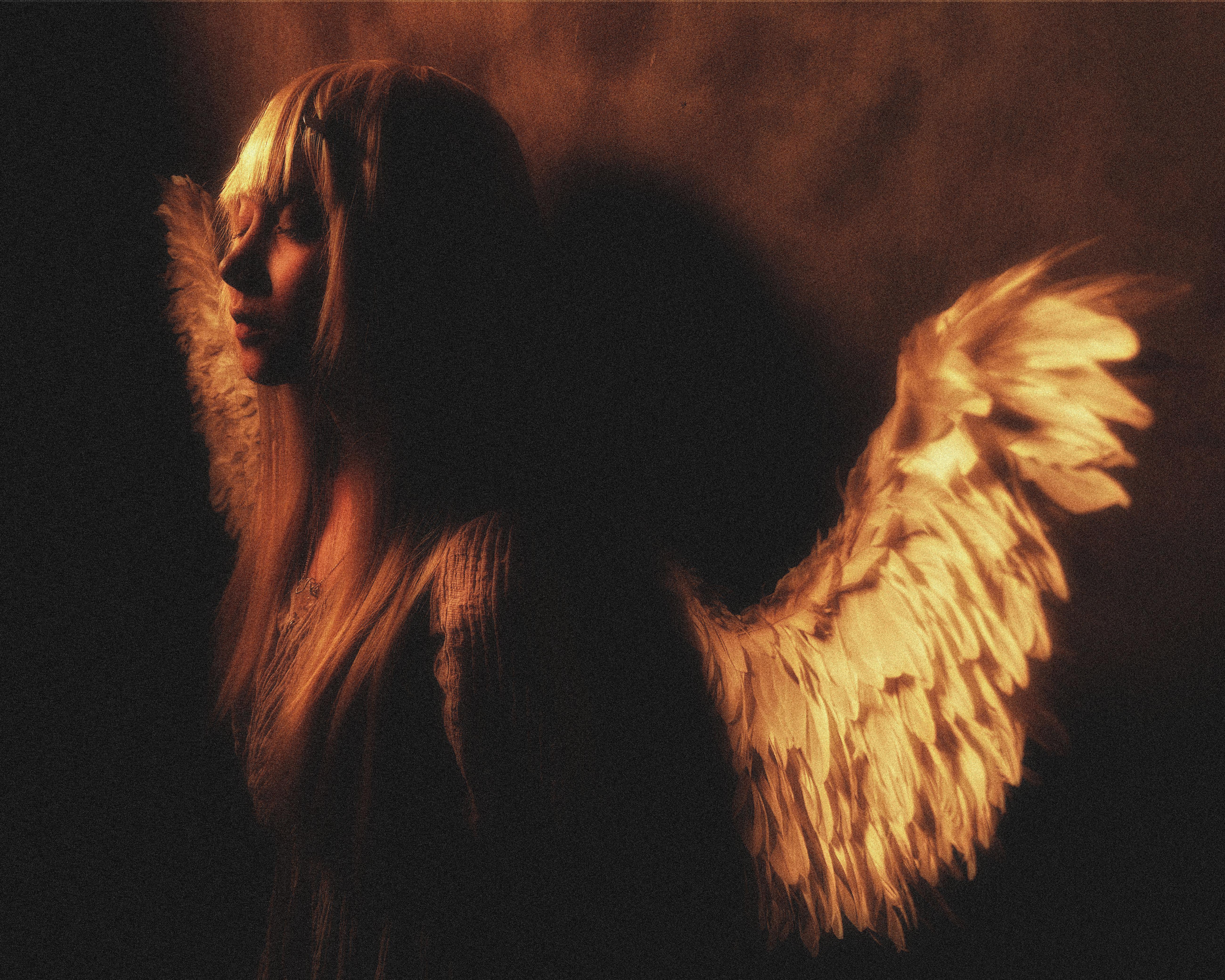 Moody portrait of an angelic figure with glowing wings, evoking mystery and serenity.