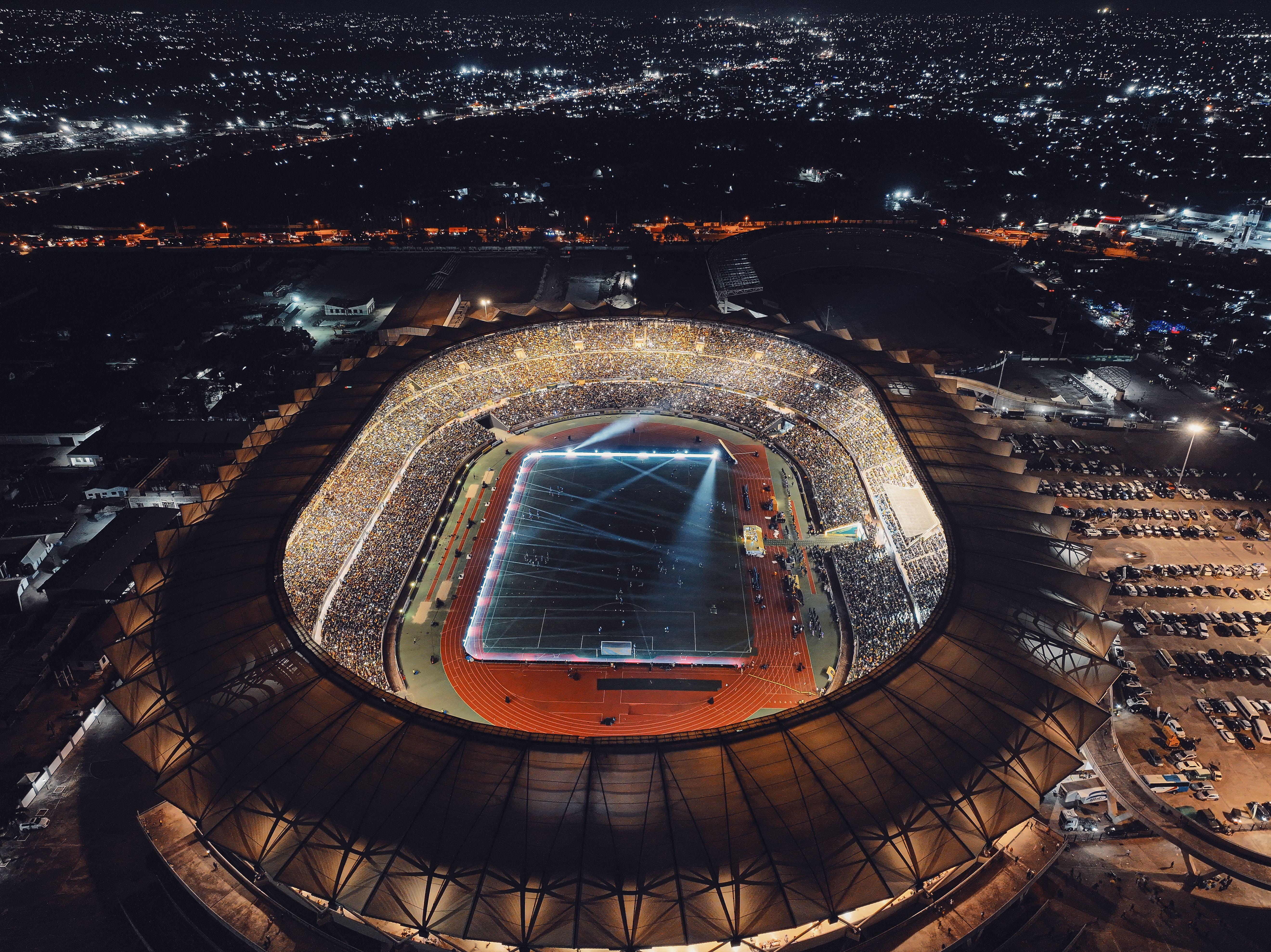 Vibrant night view of a brightly lit stadium in Dar es Salaam during a soccer match with a full crowd.
