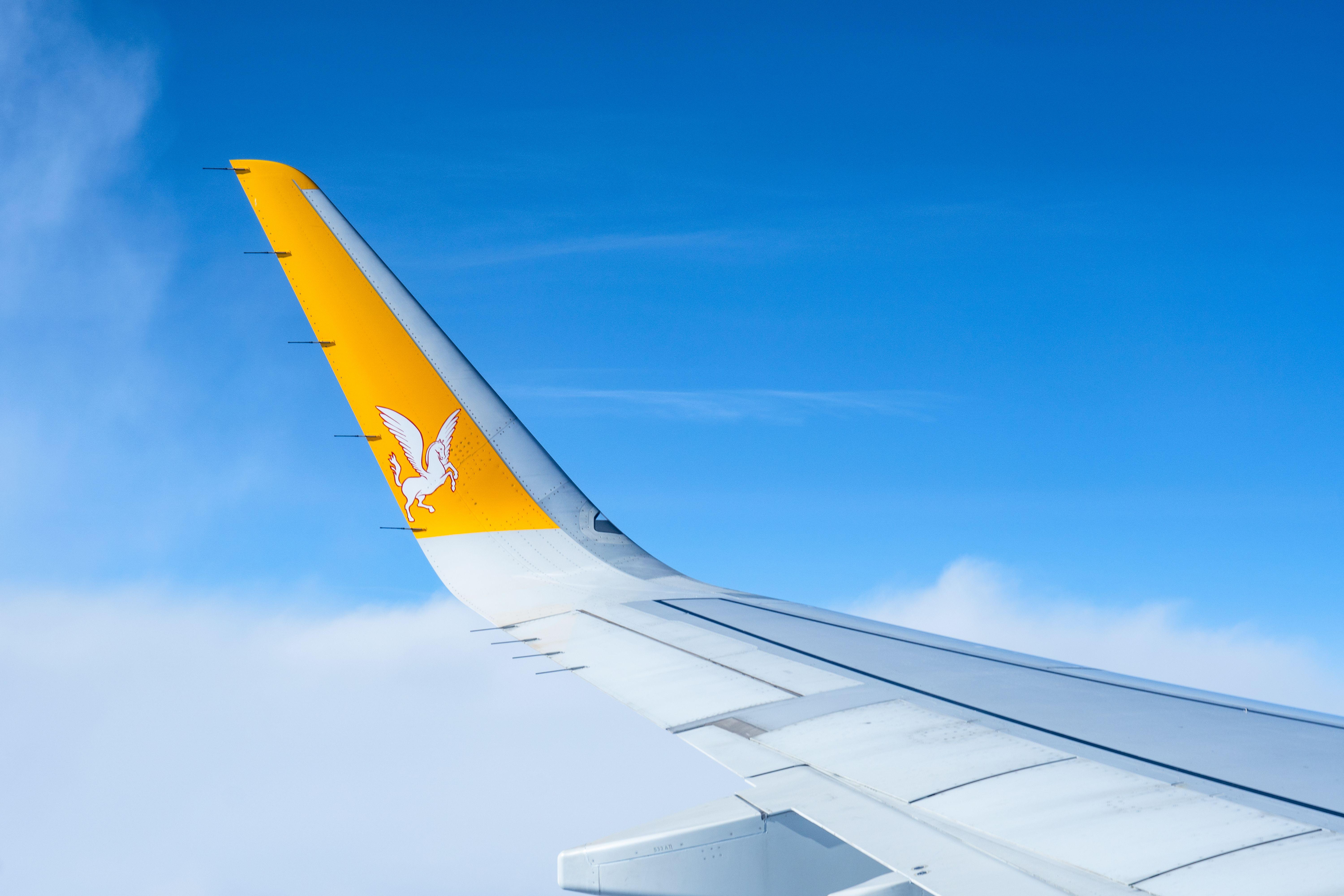 Airplane wing with airline logo flying above the clouds on a clear day.