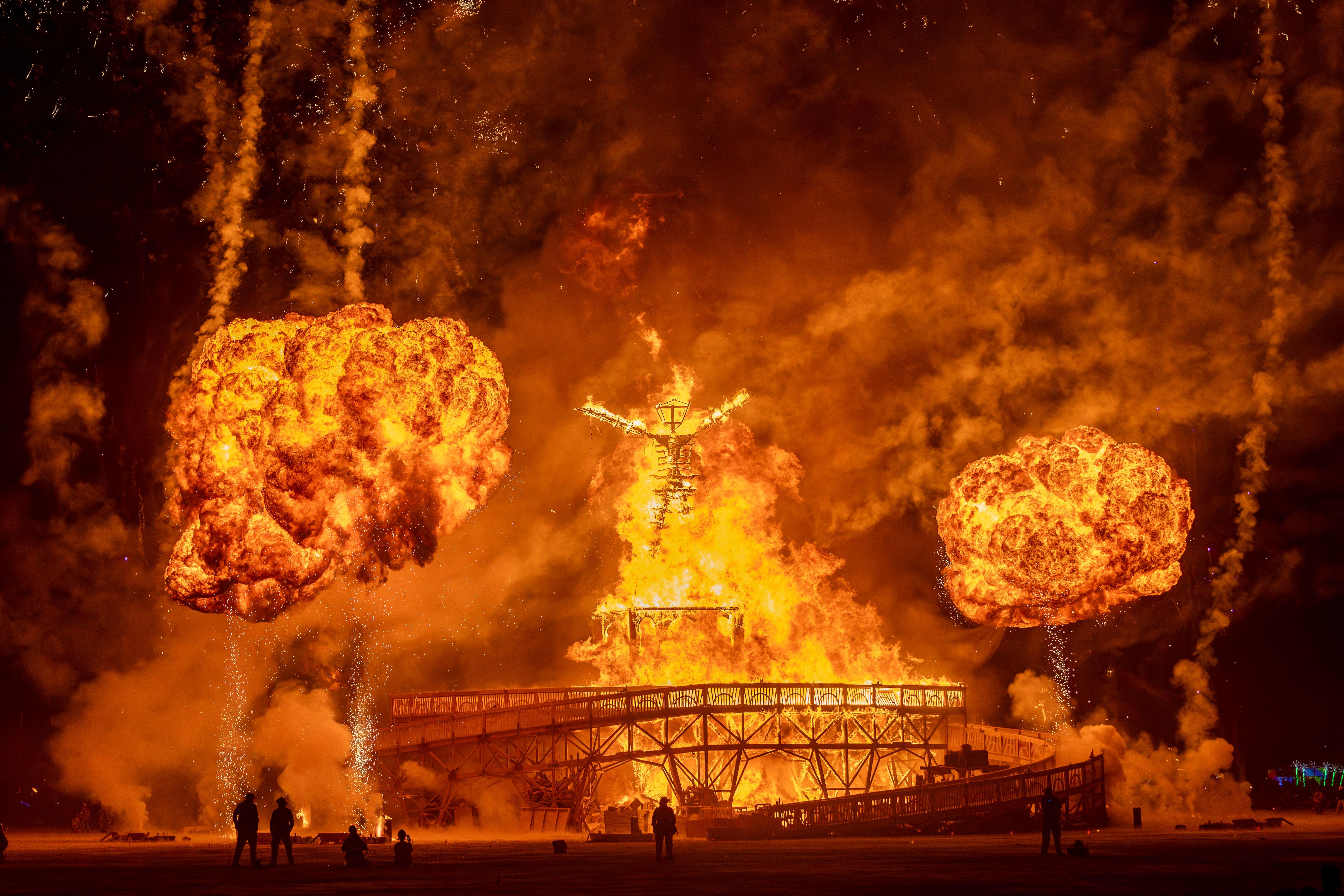 Dramatic fire and fireworks display at Burning Man festival with glowing effigy silhouette.