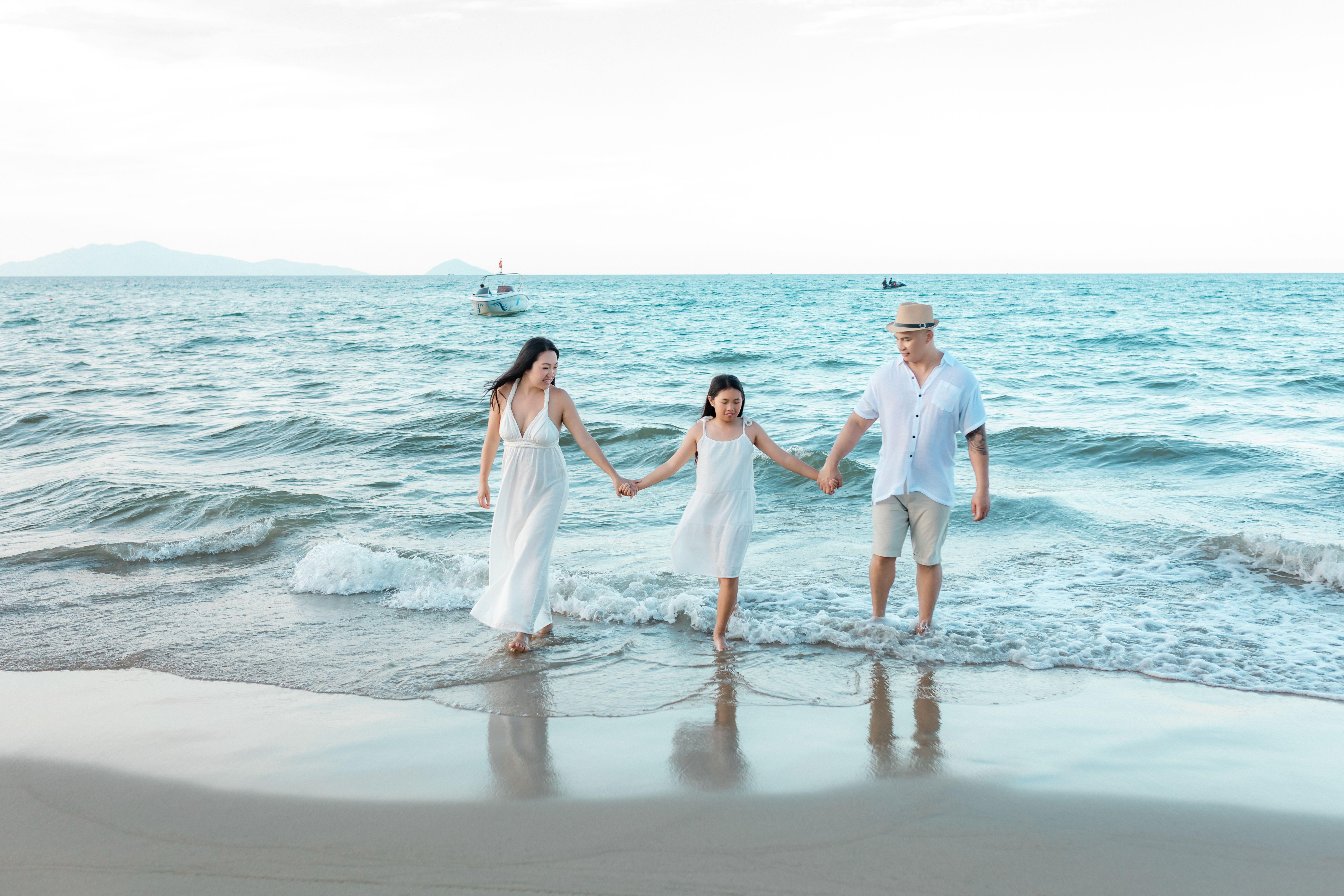 A joyful family of three walks hand-in-hand along Hội An beach, enjoying a sunny day.