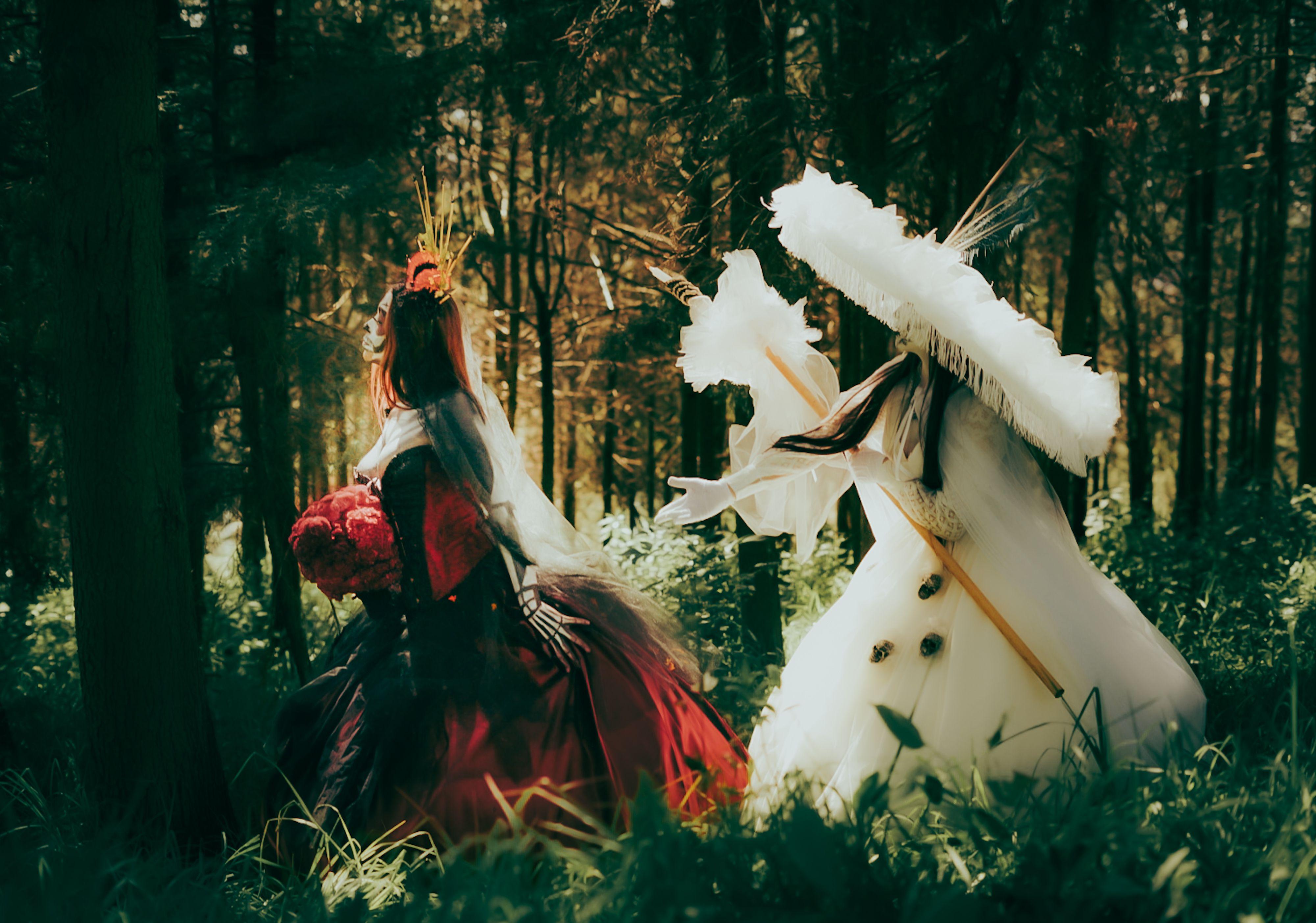 Two people in elaborate costumes explore an enchanting forest setting, creating a whimsical fairytale atmosphere.