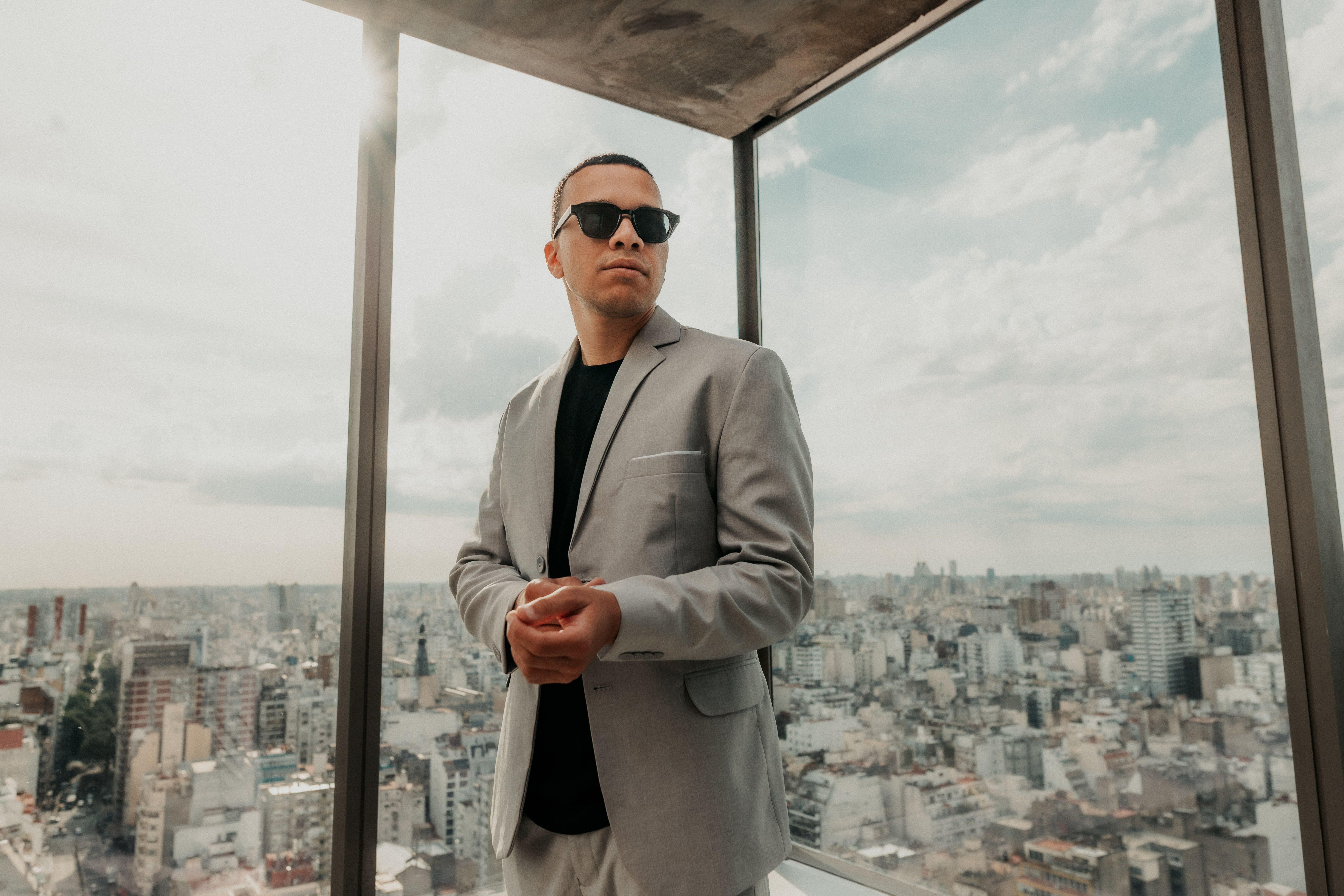 Confident man in a suit with sunglasses overlooking Buenos Aires cityscape from a modern office building.