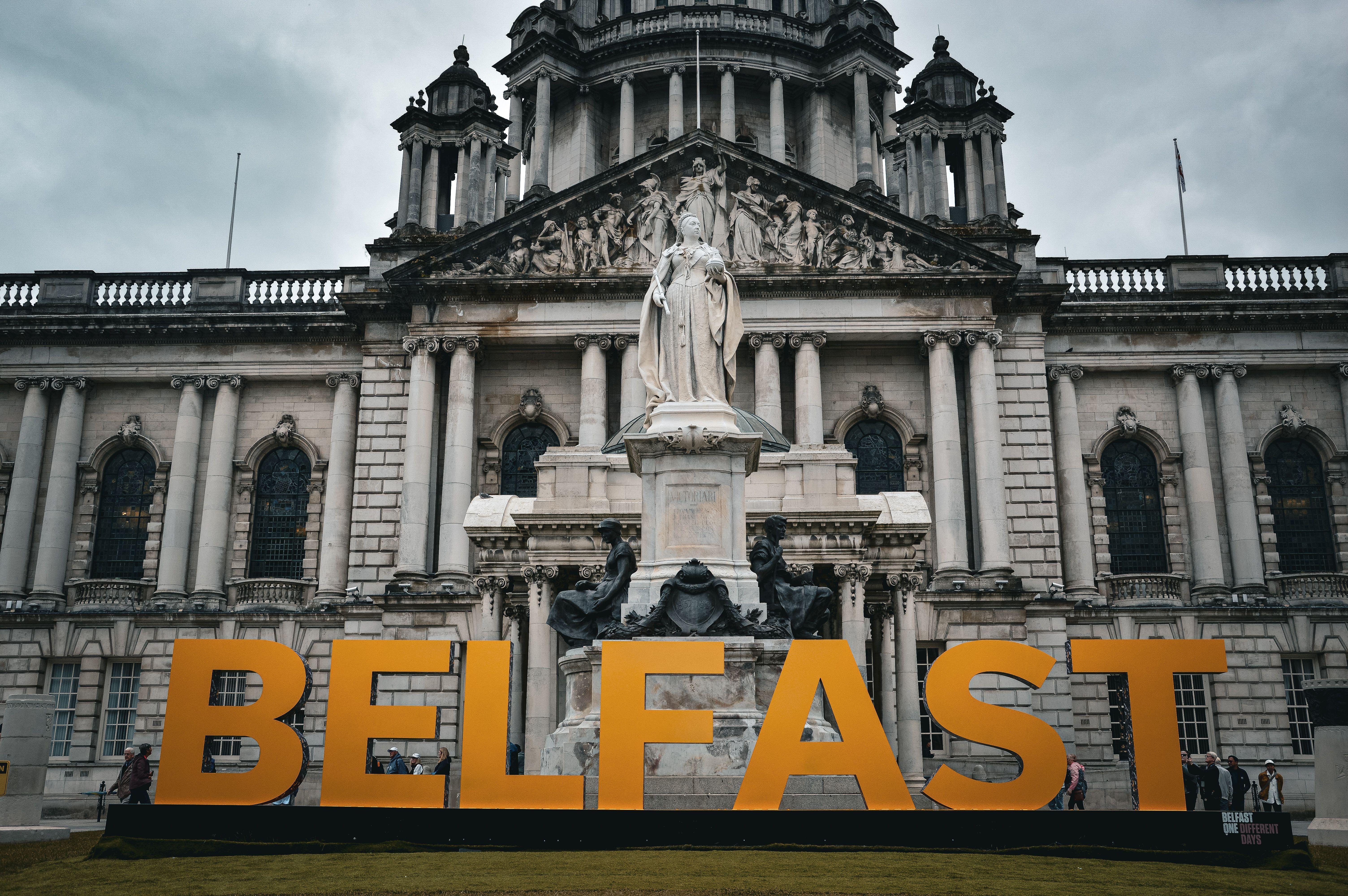 View of the Belfast City Hall with striking statue and Belfast sign, showcasing historical architecture.