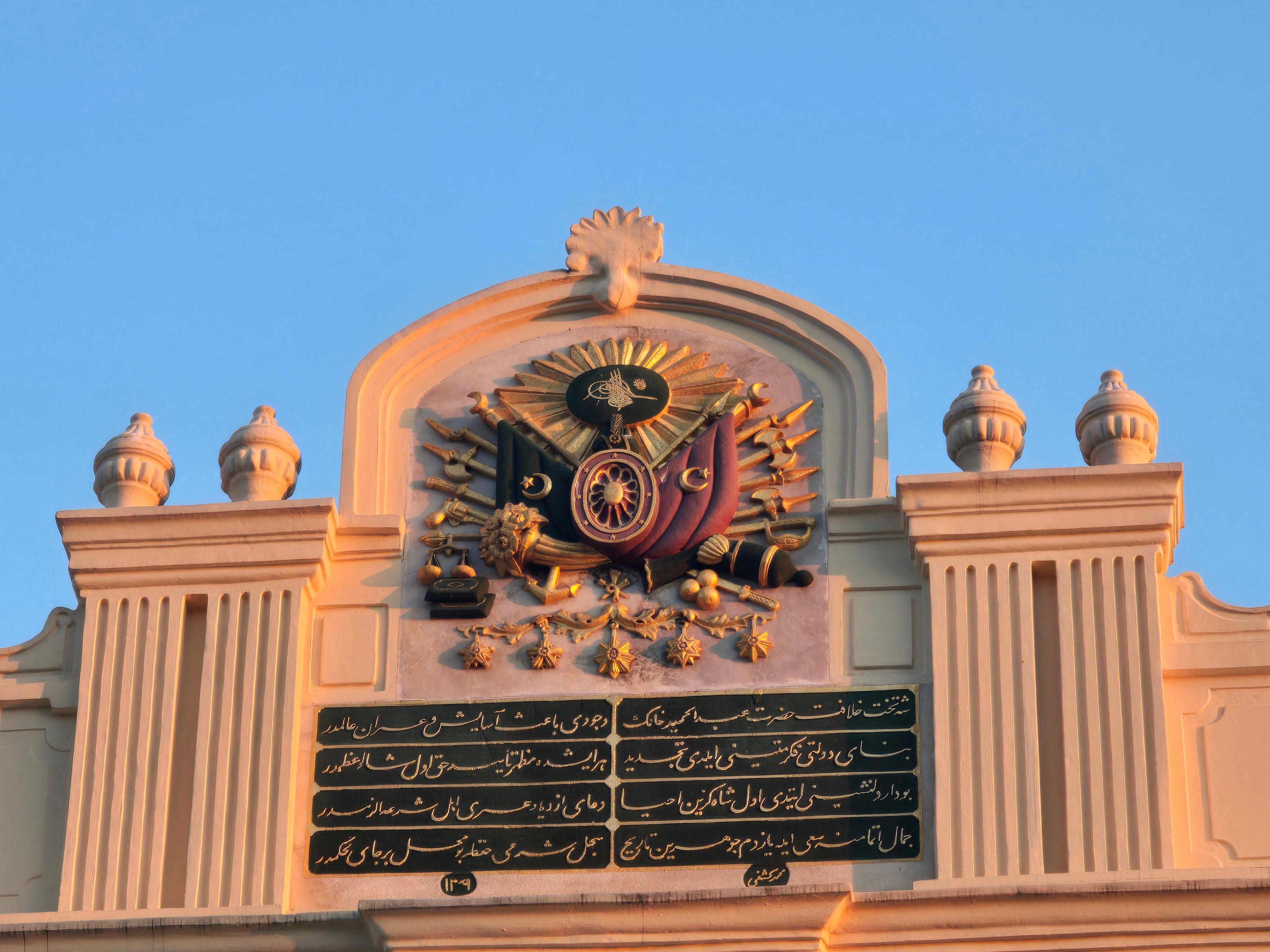 Detailed view of Ottoman Empire insignia on a historical building facade during sunset.