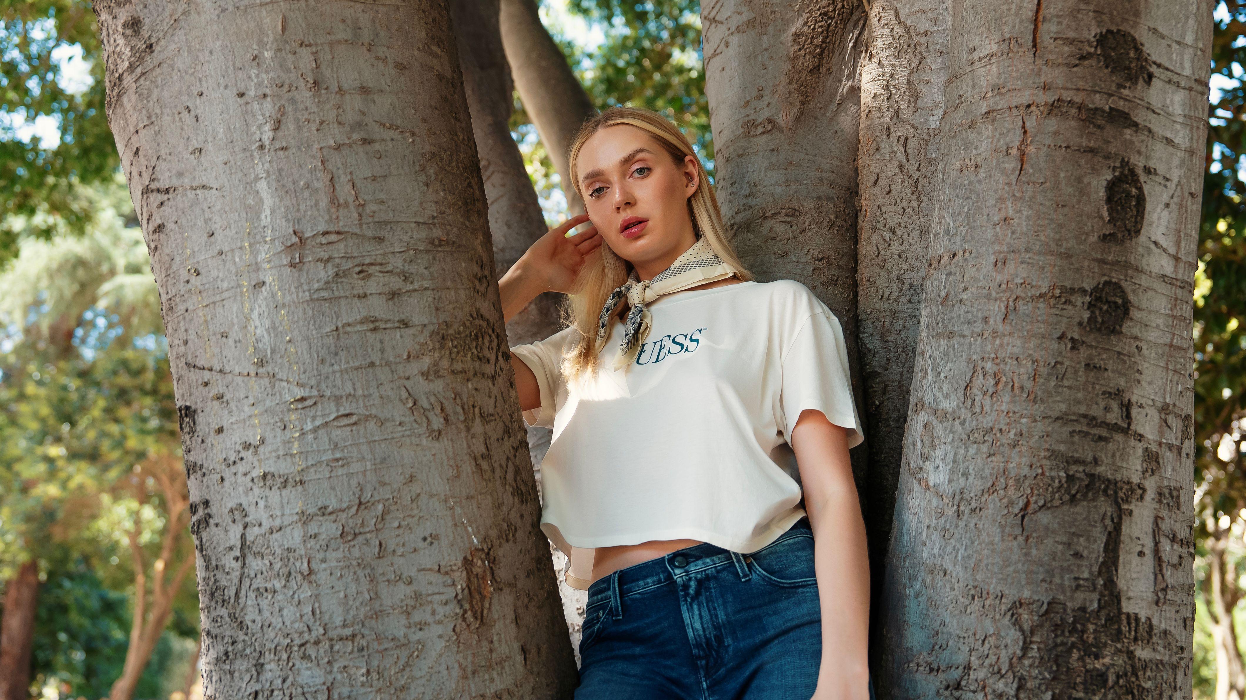 Stylish woman posing between trees in a serene outdoor environment, embracing nature.