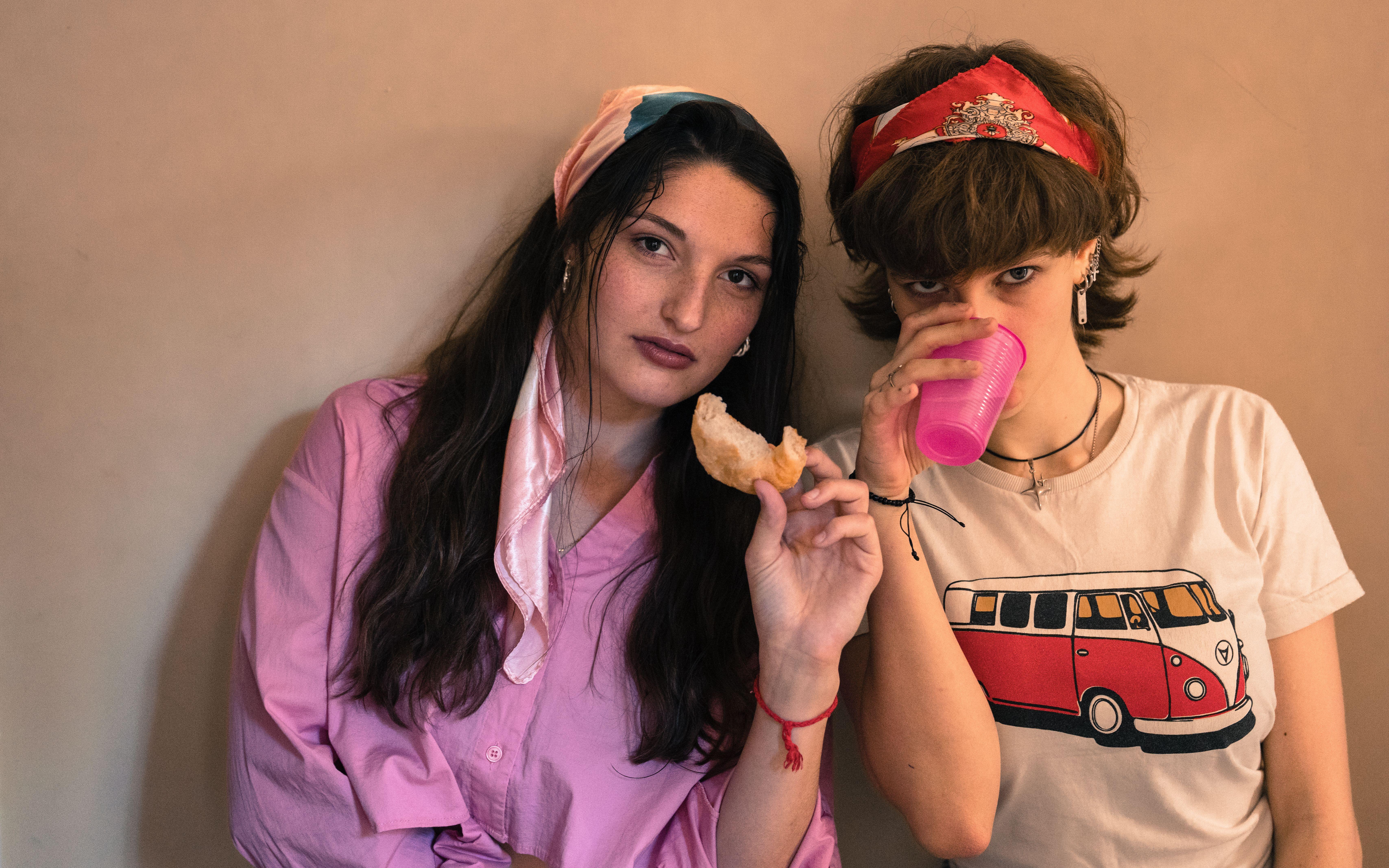 Two stylish young women indoors with a snack and pink drink. Casual and vibrant atmosphere.