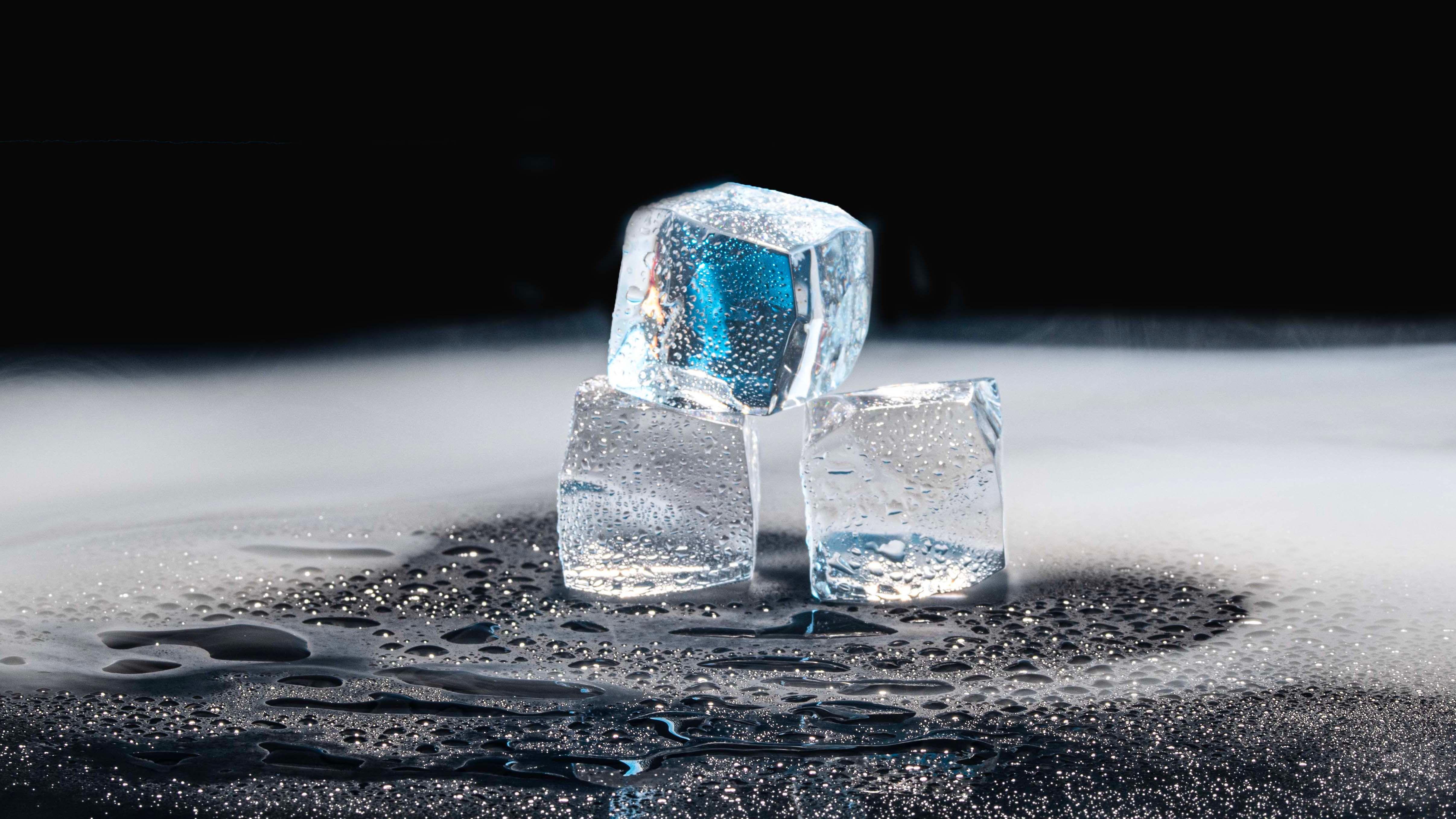 Three ice cubes melting on a black surface with water droplets.