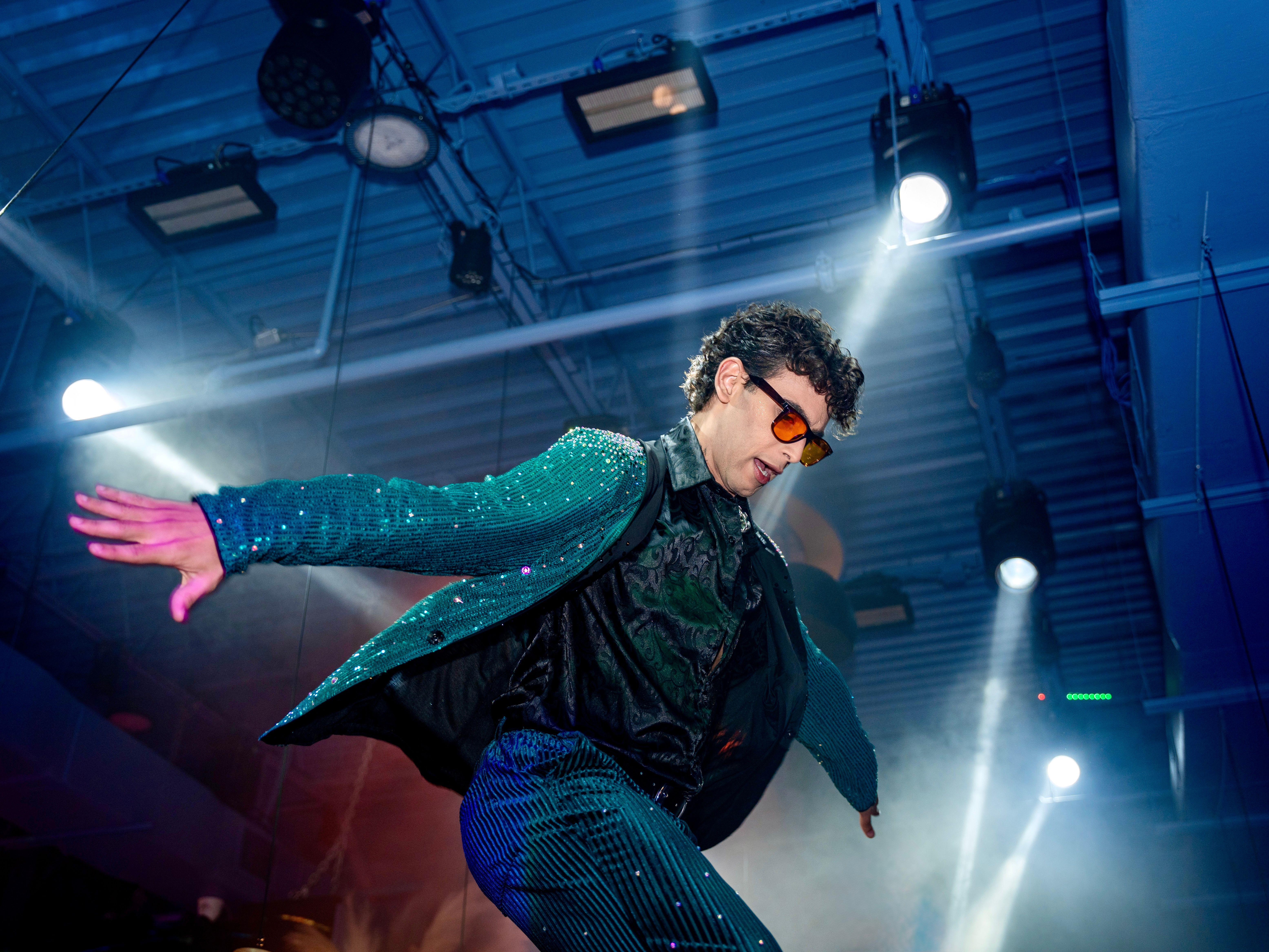 Energetic performer in vibrant clothing dances under spotlights in a lively indoor setting.
