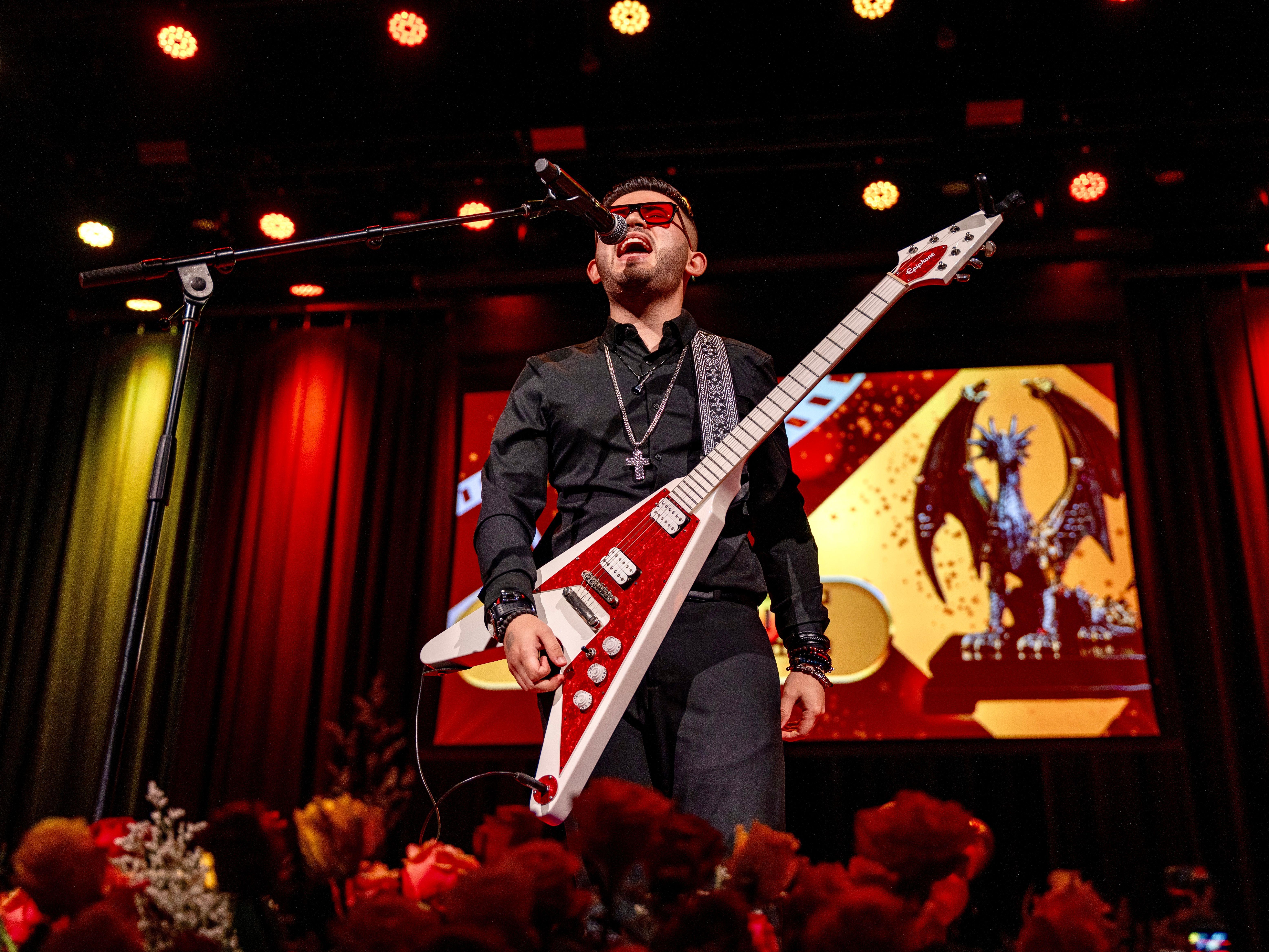 Energetic rock musician performing on stage with electric guitar and microphone under vibrant lights.