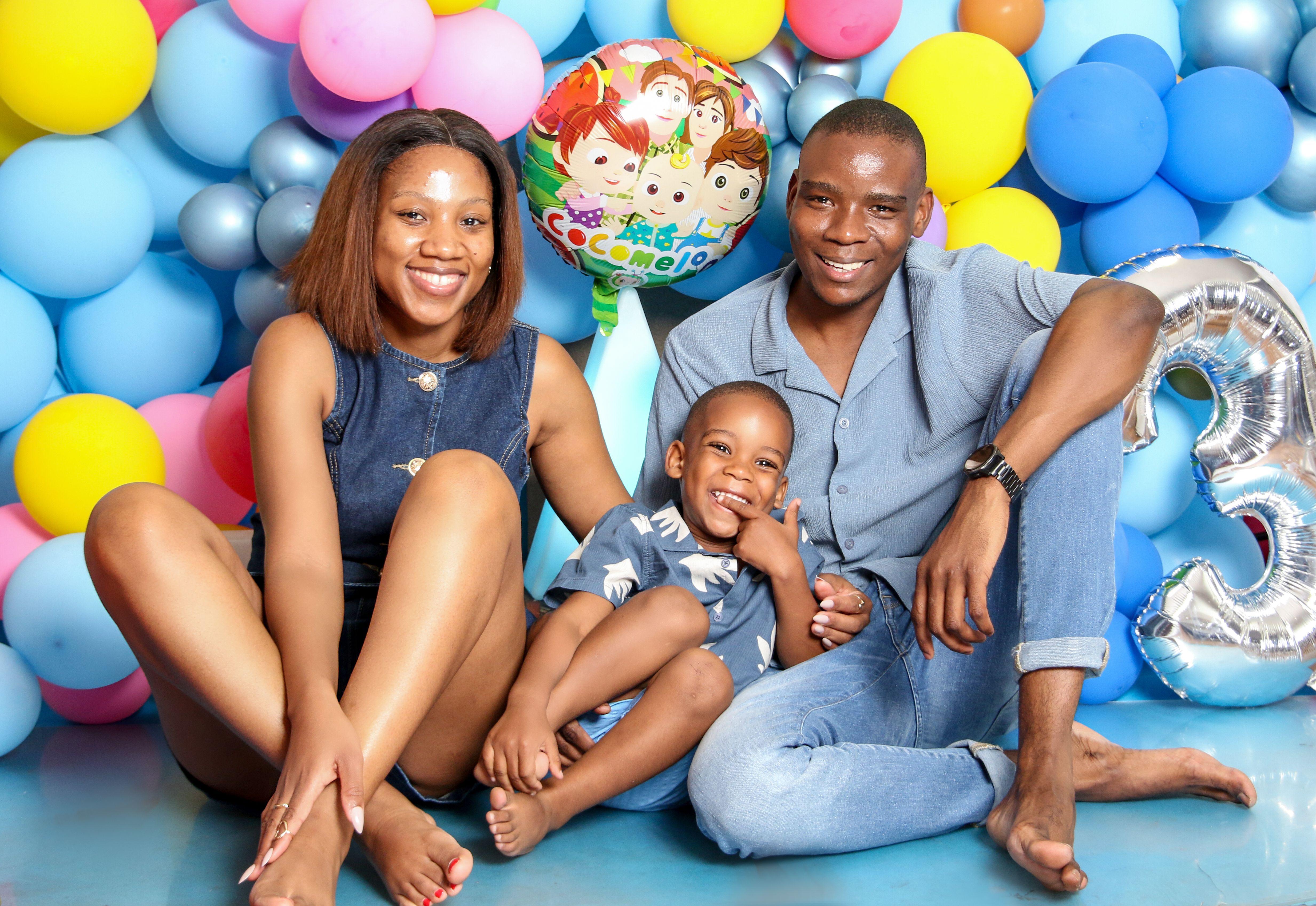 A happy family celebrating a child's birthday surrounded by colorful balloons.