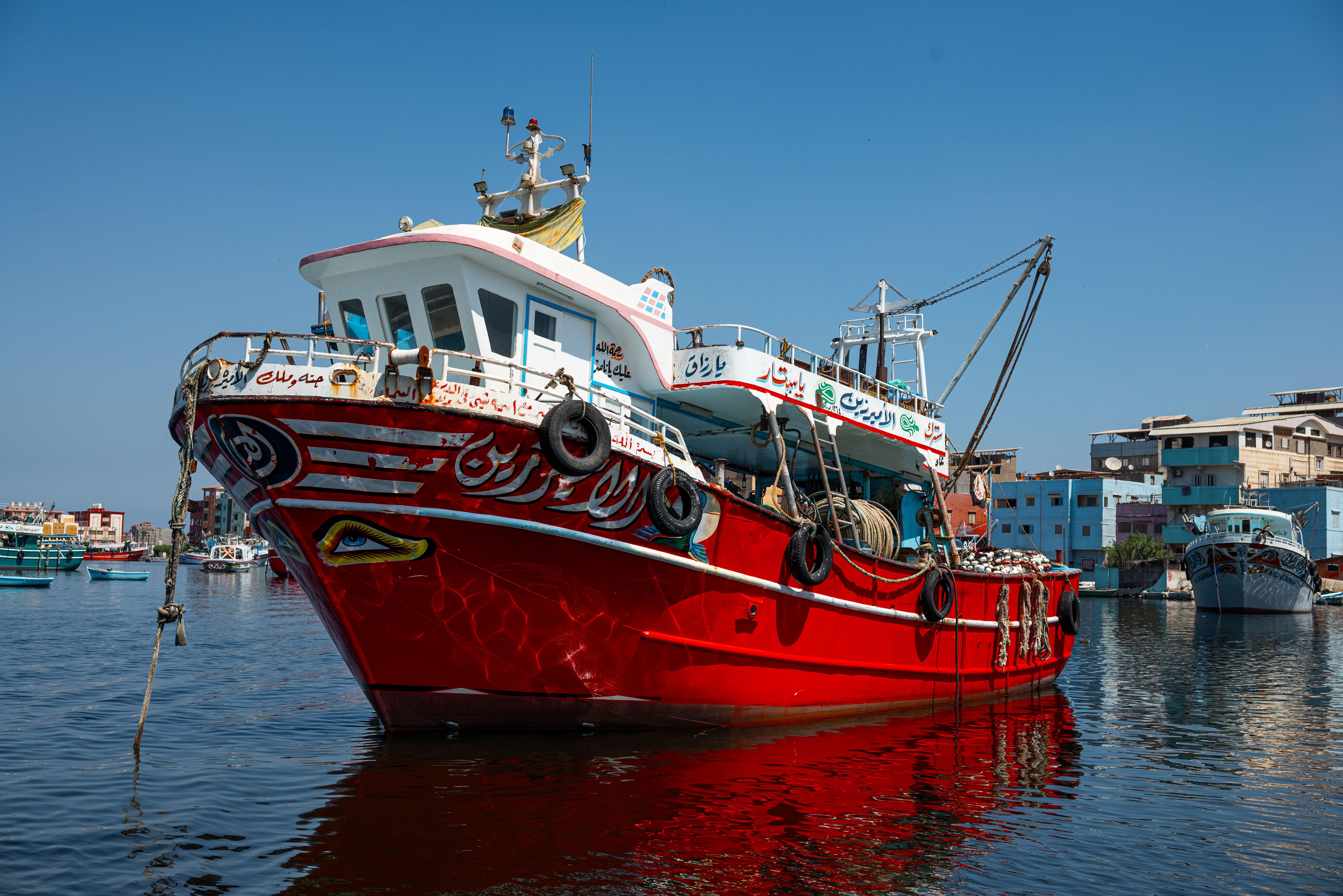 A striking red fishing boat docked in a sunny harbor with clear blue skies.