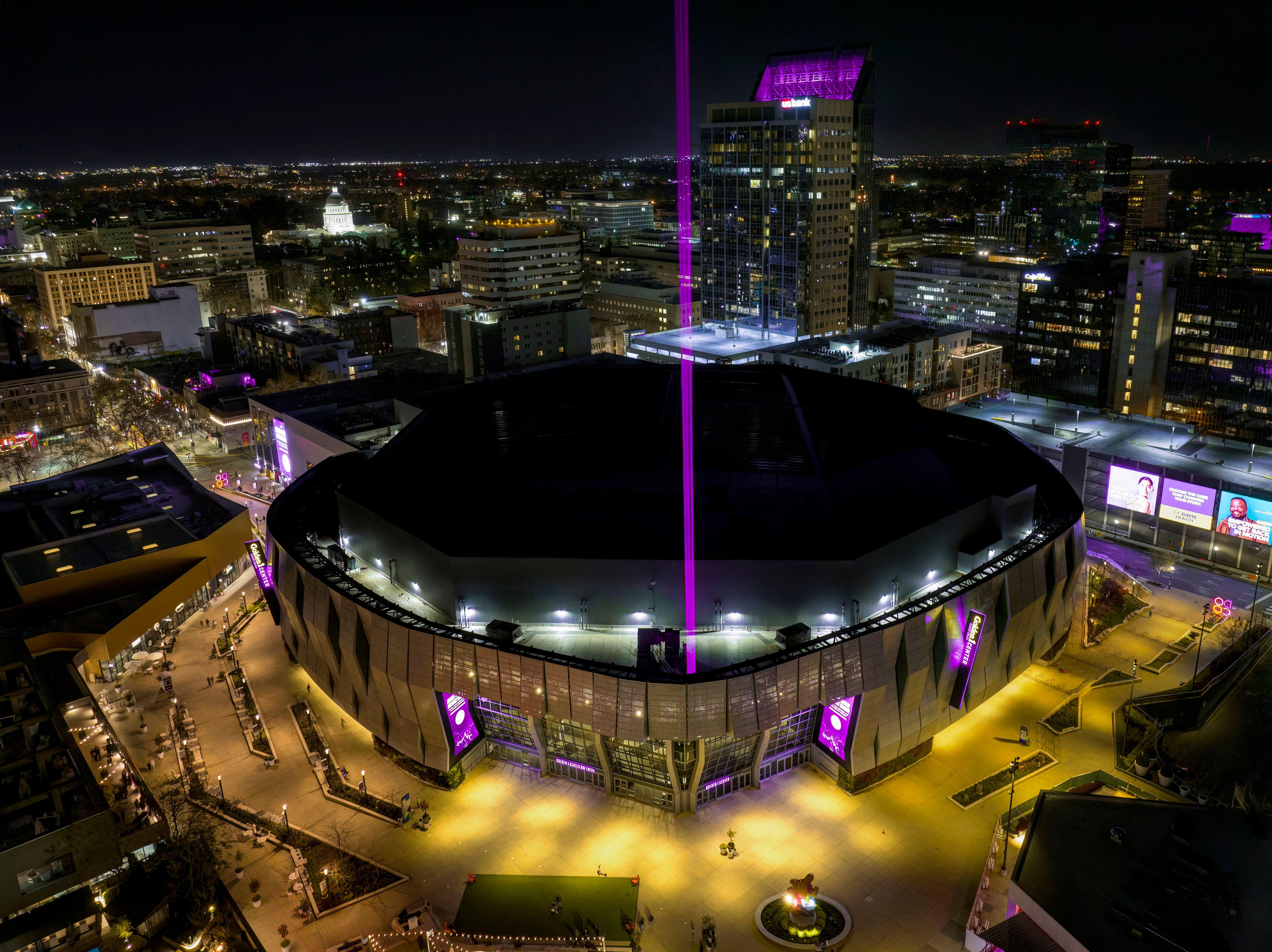 Aerial view of Golden 1 Center in downtown Sacramento illuminated at night with vibrant purple lights.