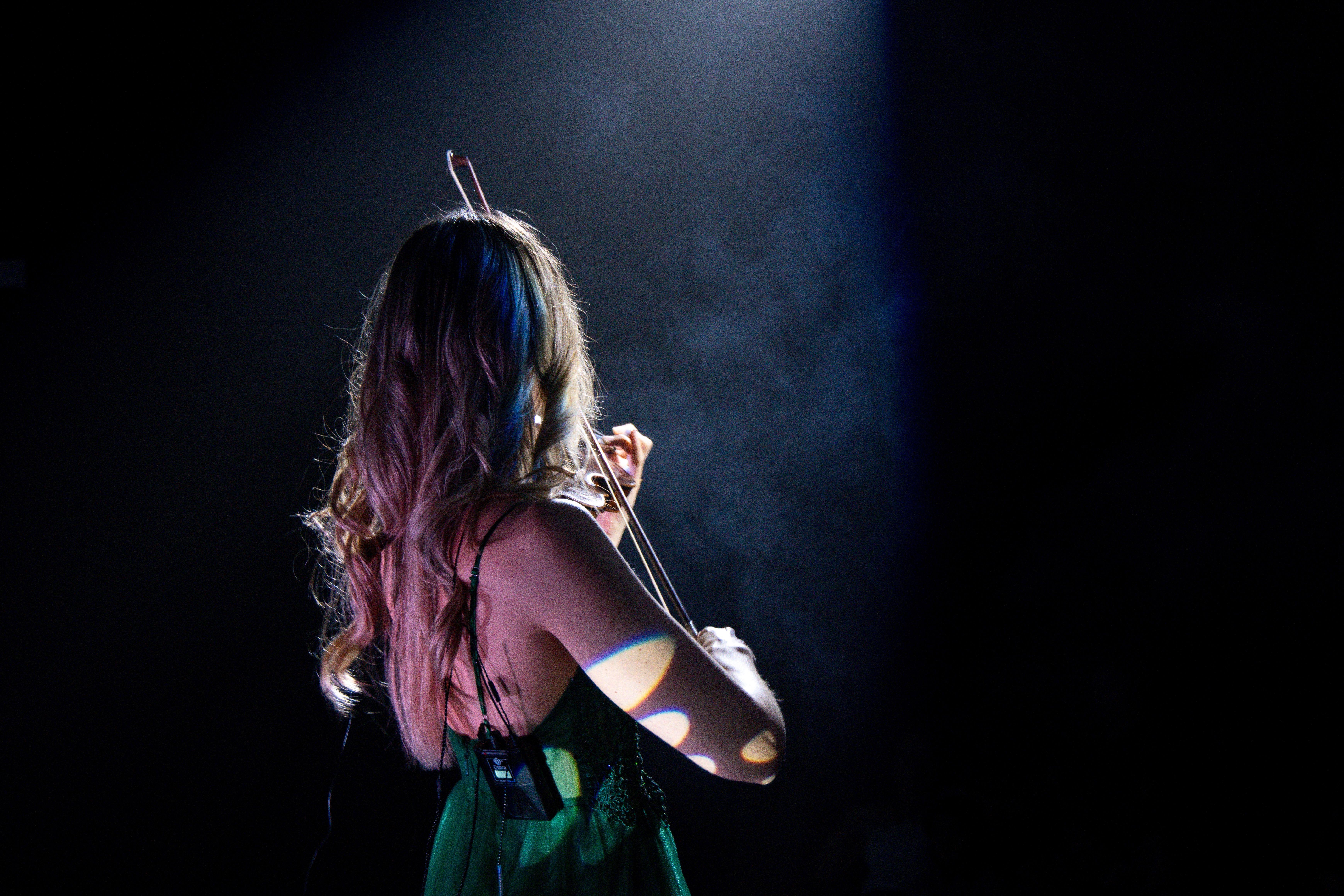A female violinist in a green dress plays passionately under a spotlight.