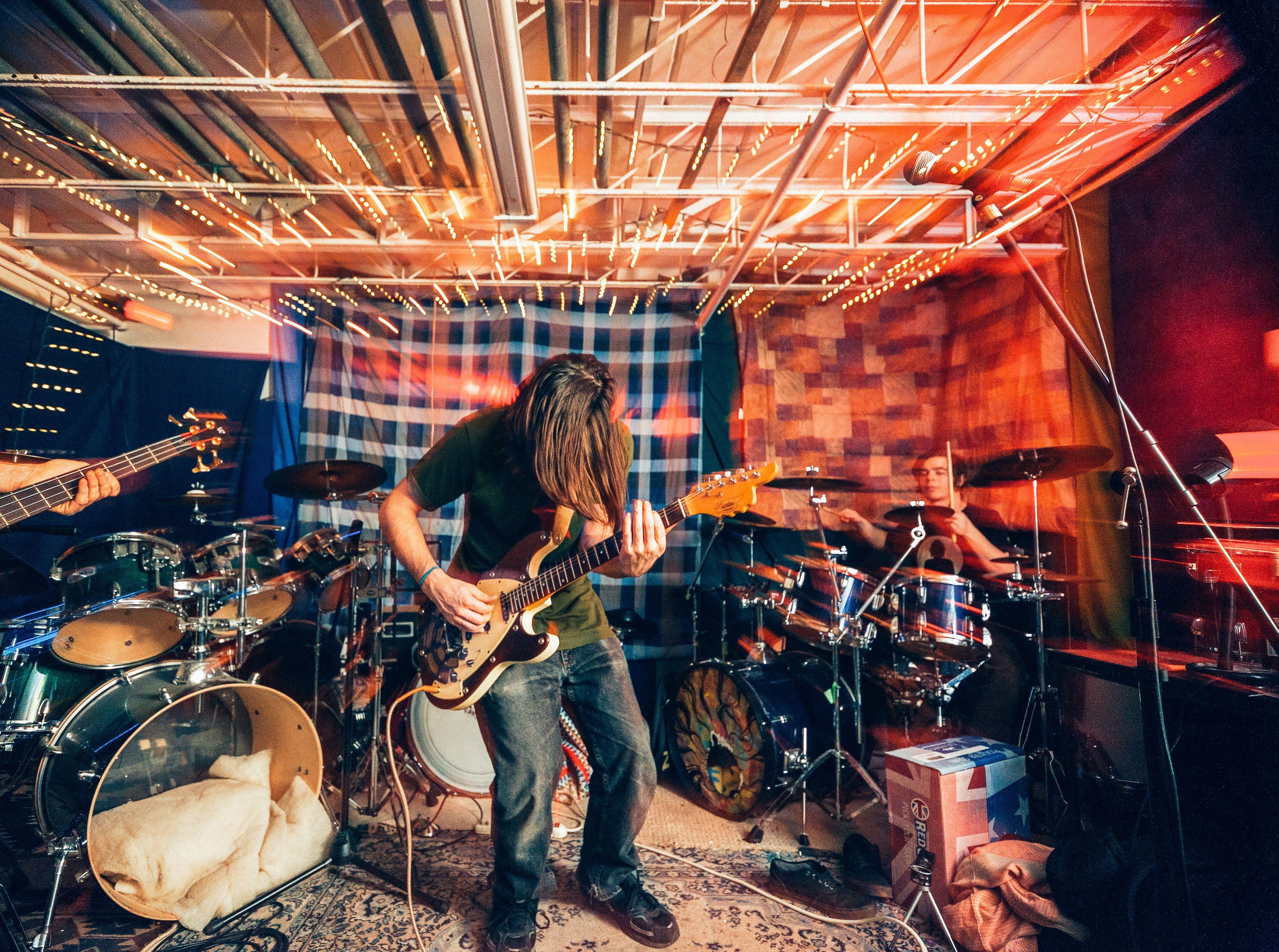 Energetic rock band performance with electric guitar and drums under colorful lights indoors.