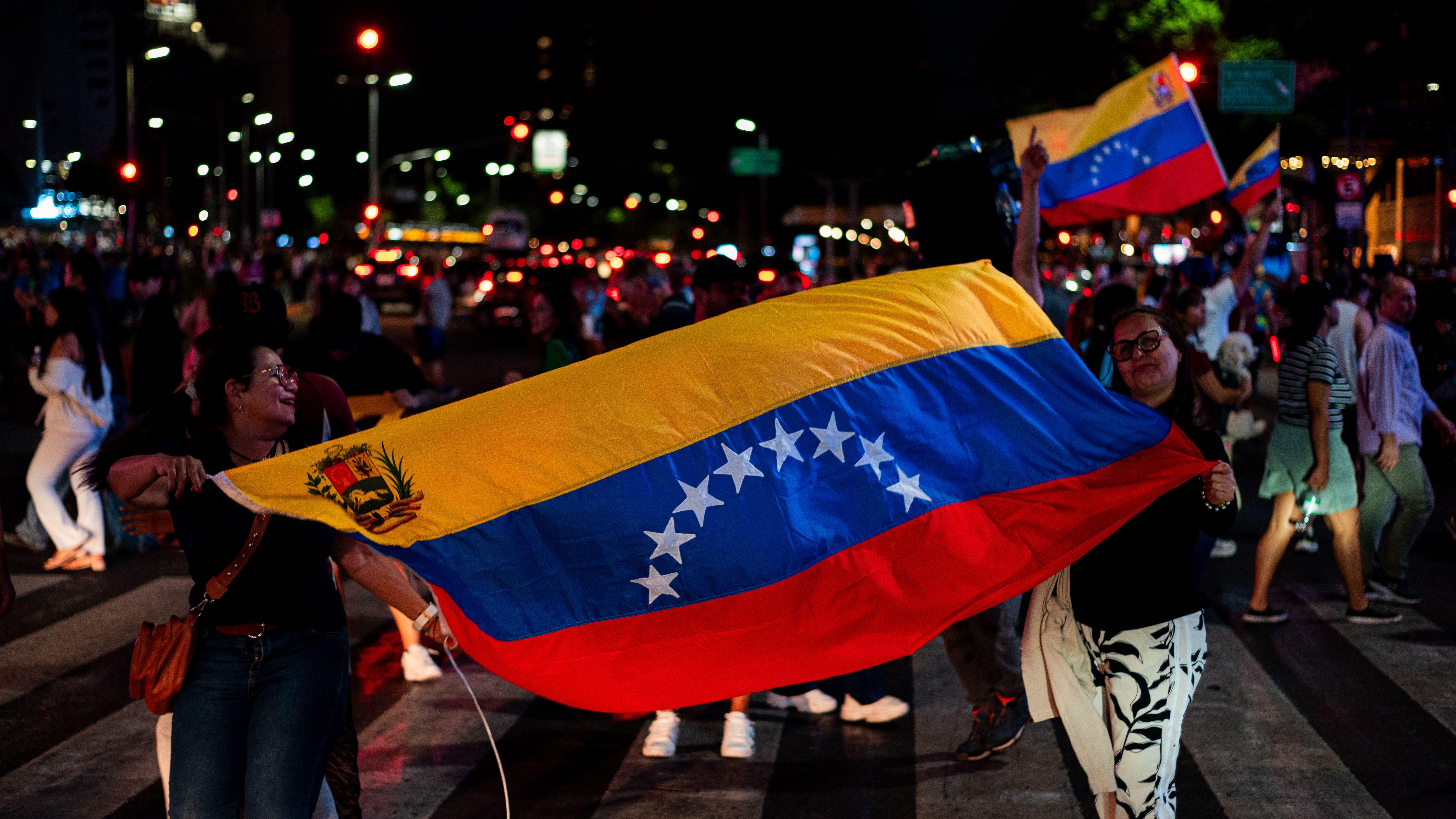 Venezuelans celebrating with national flags on a busy street in Buenos Aires at night.