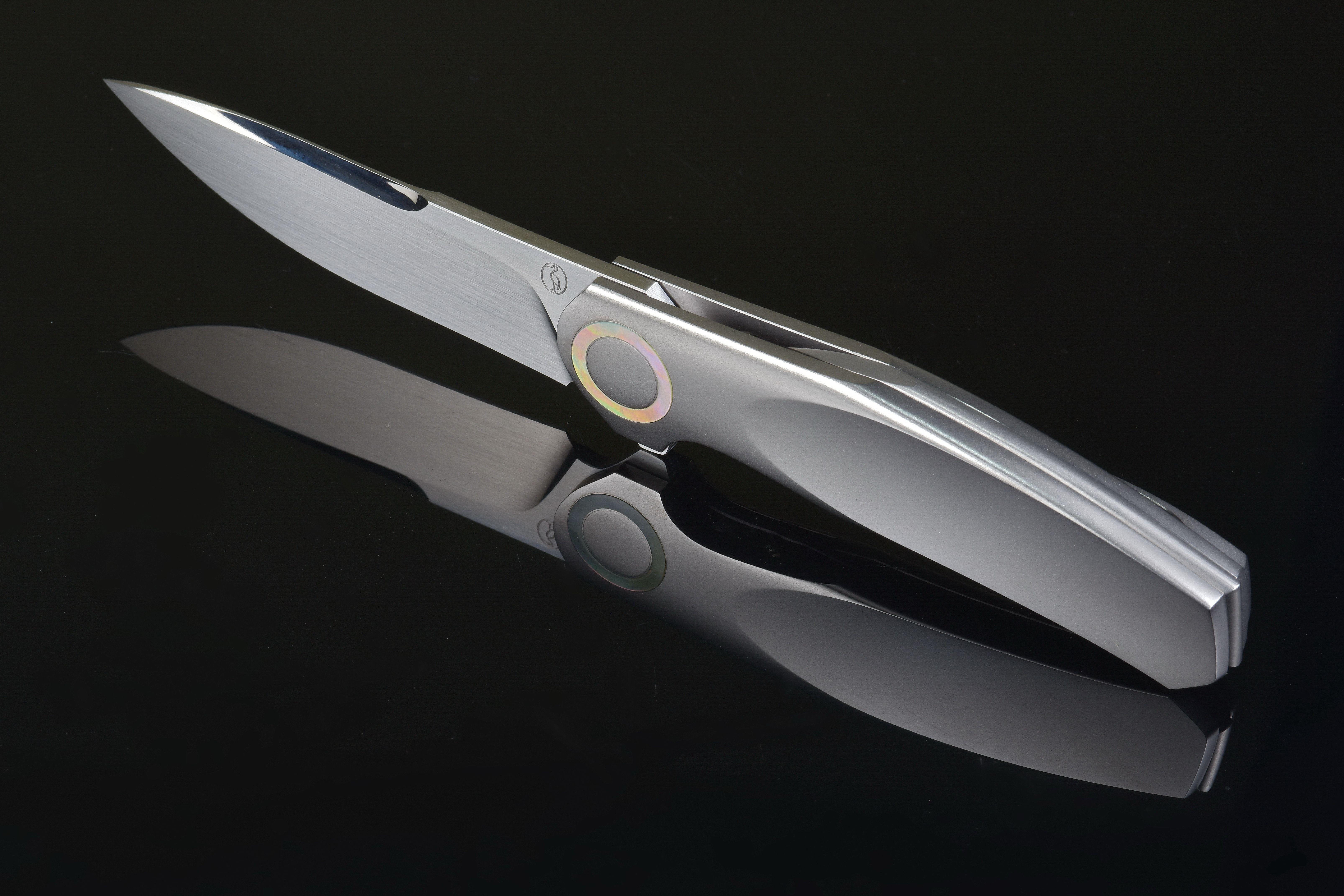 Elegant silver folding knife on a dark reflective background, showcasing modern design and craftsmanship.