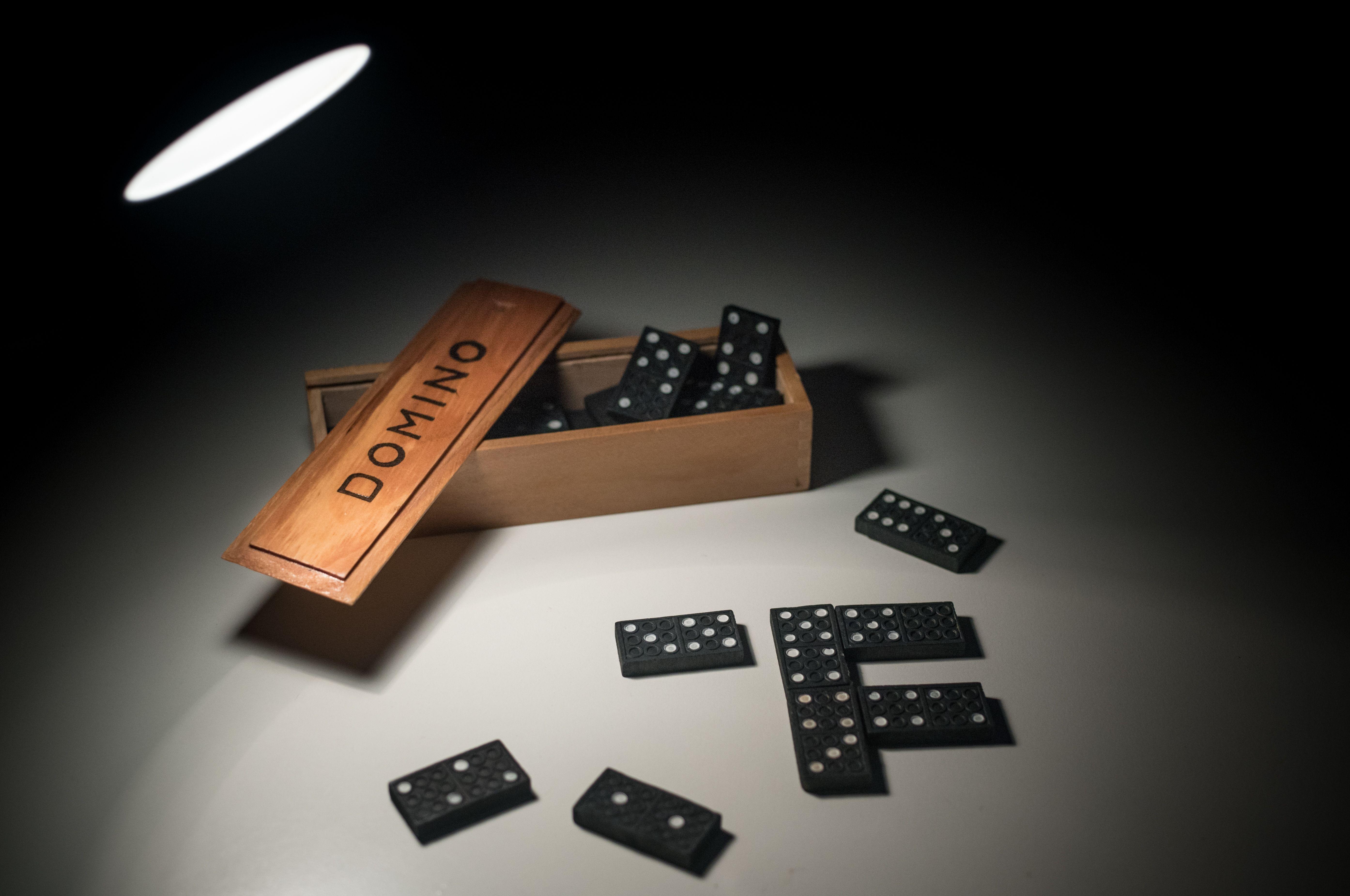 Black domino pieces spilling from a wooden box under dramatic lighting, highlighting a classic game setup.