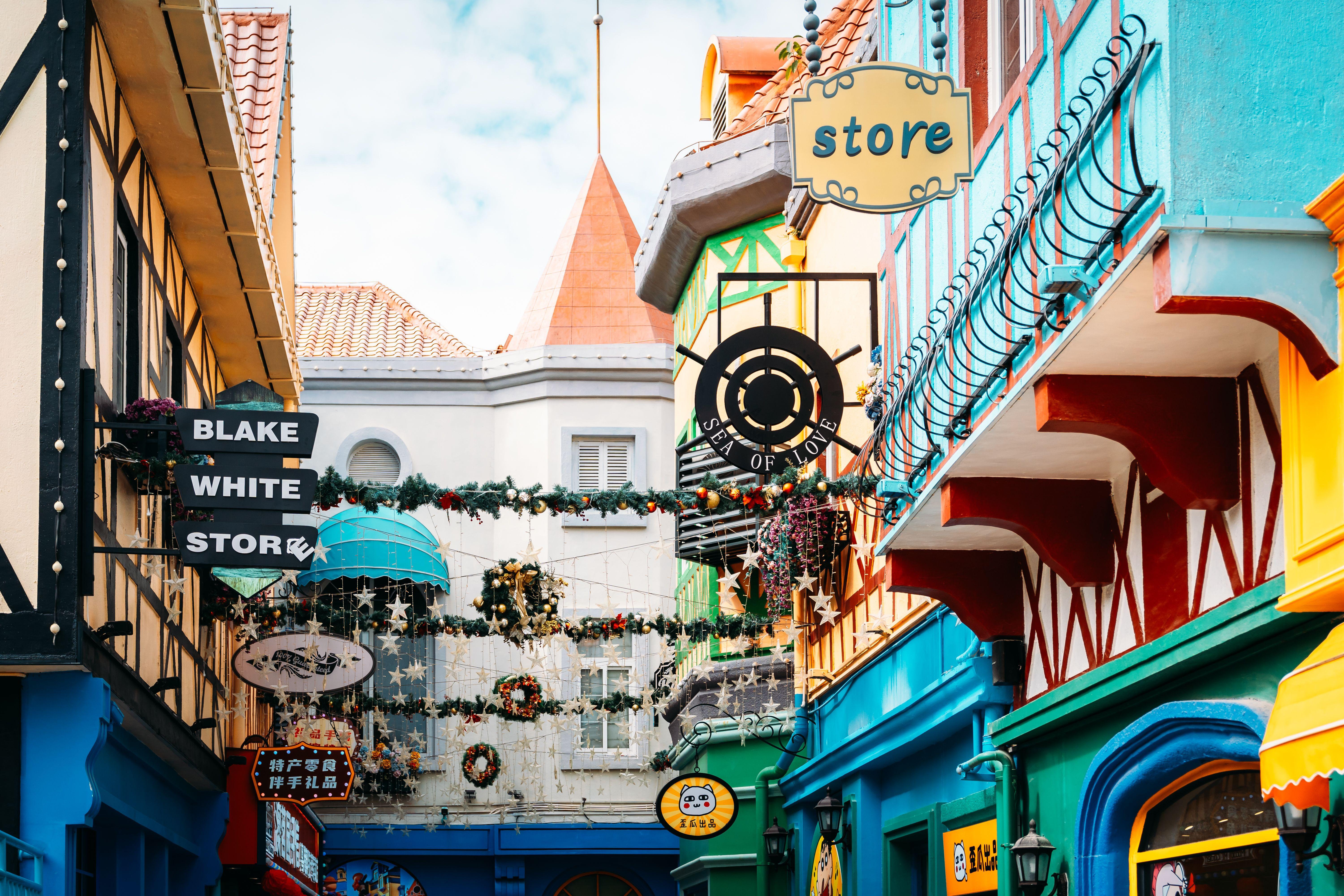 A festive shopping street adorned with colorful storefronts and holiday decorations under a bright sky.
