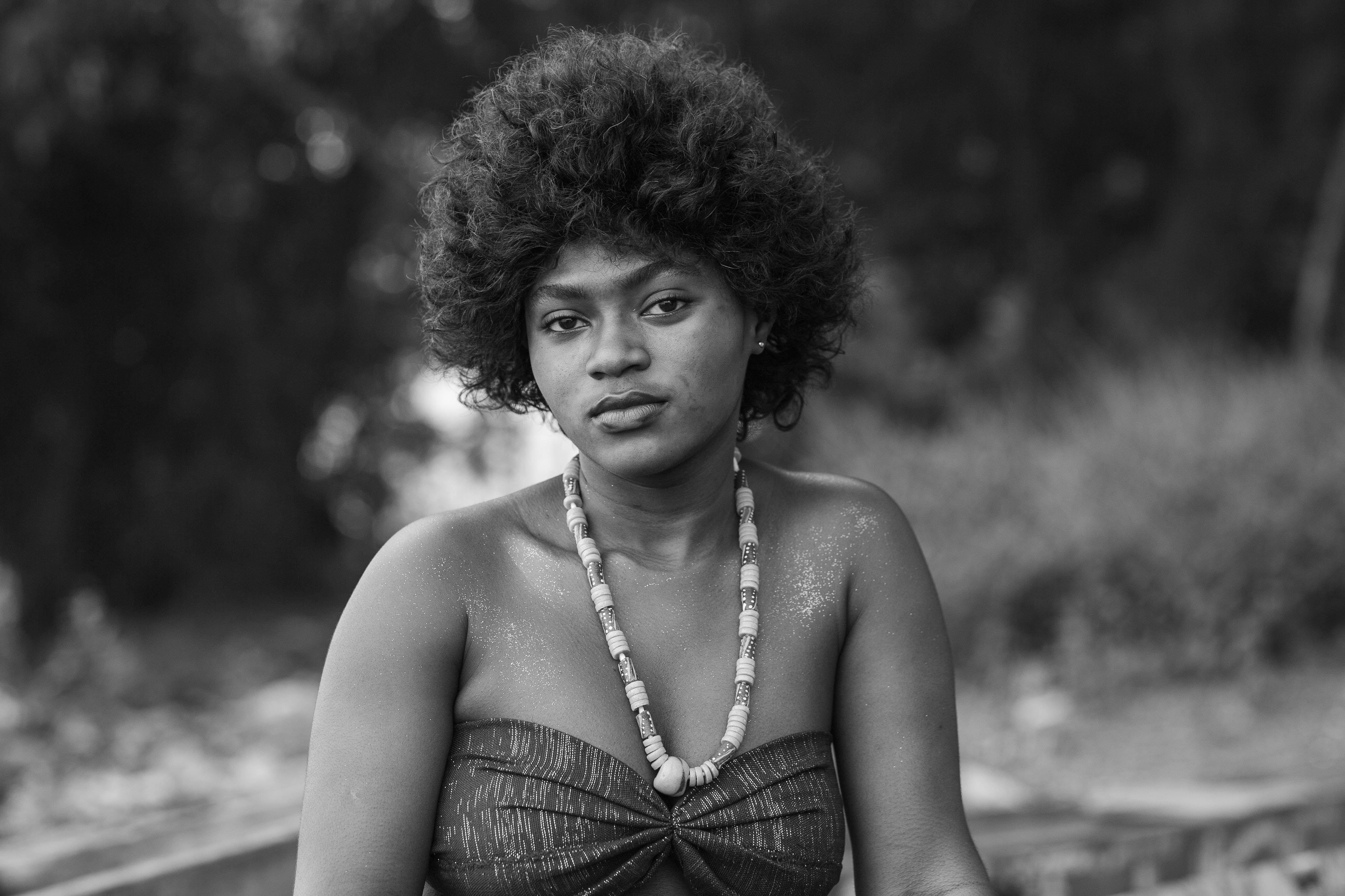 Black and white portrait of a woman with a natural hairstyle and traditional African necklace outdoors.