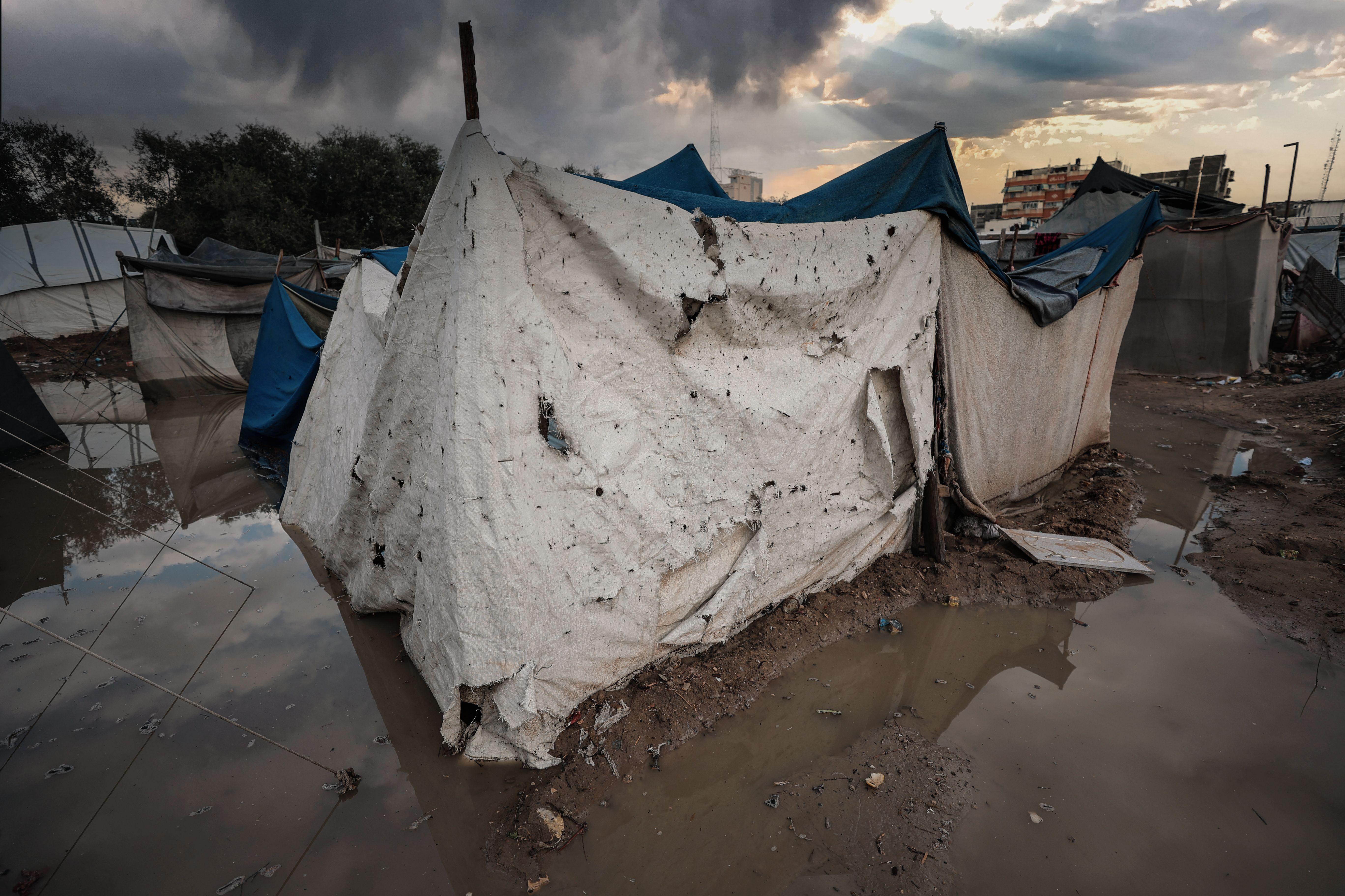 A damaged tent shelter in a flooded area of a Gaza refugee camp under stormy skies.