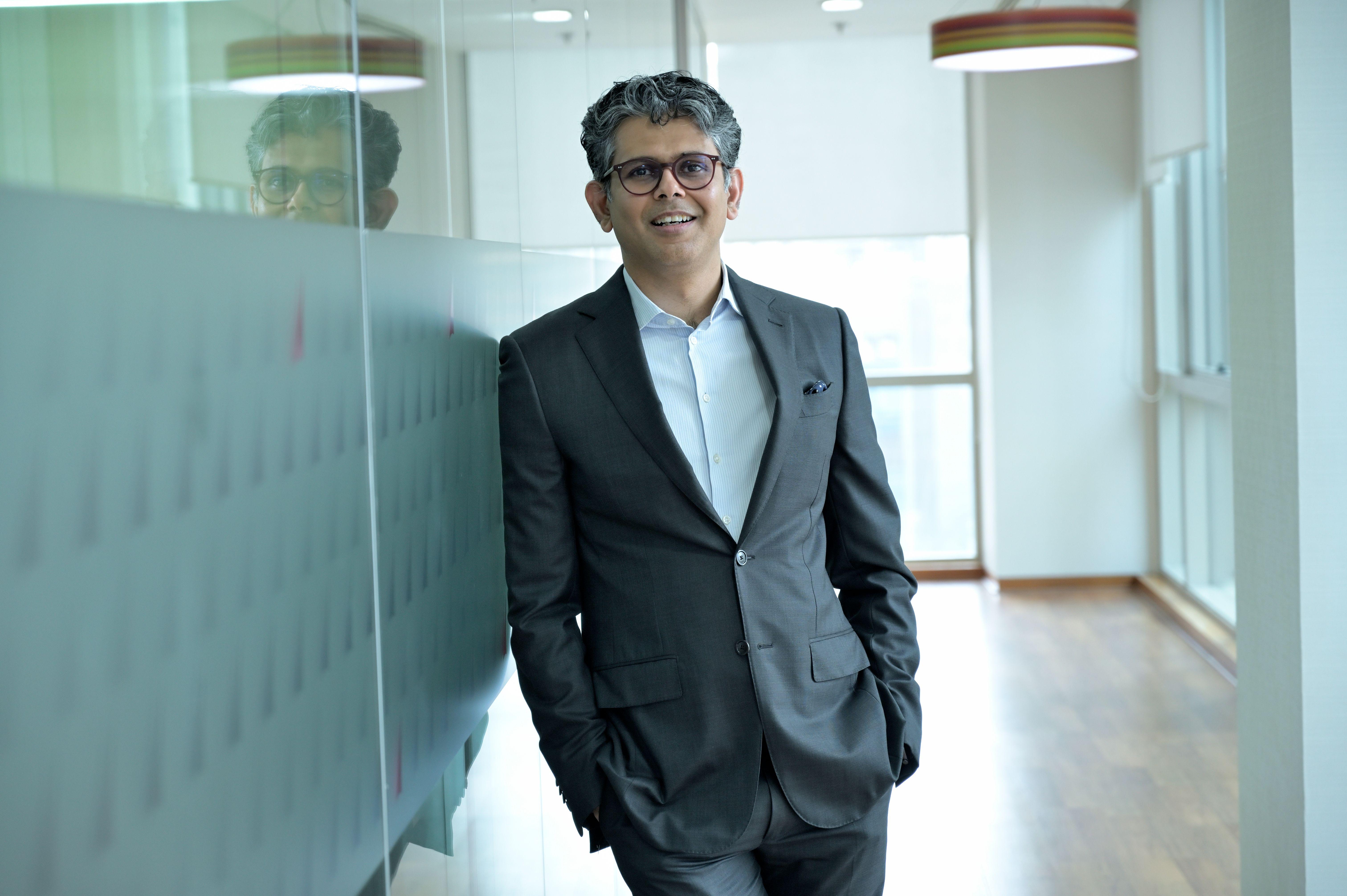 Smiling businessman standing confidently in a modern office hallway, wearing a suit.