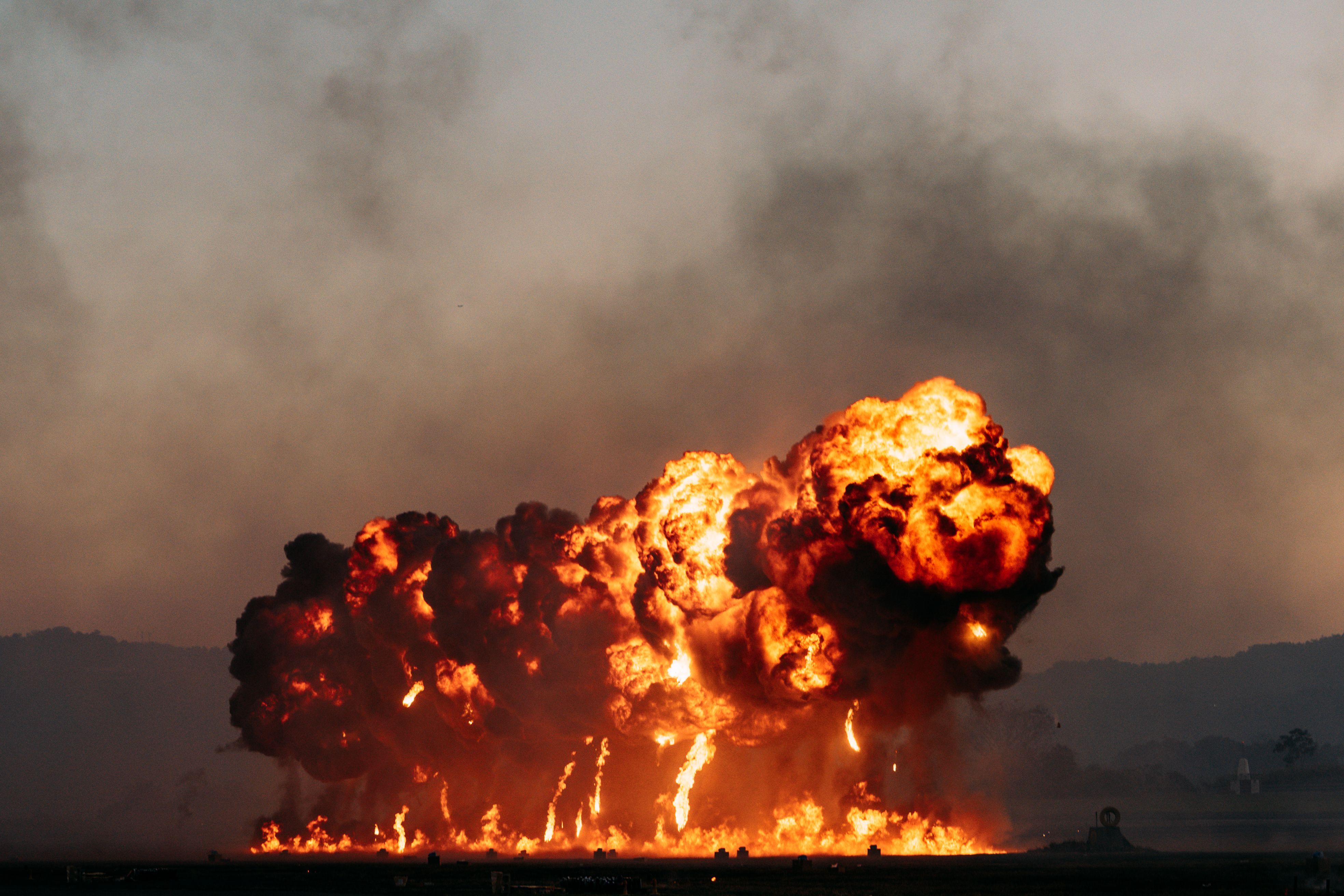 A powerful explosion with intense flames and smoke in an open field during dusk, creating a dramatic scene.