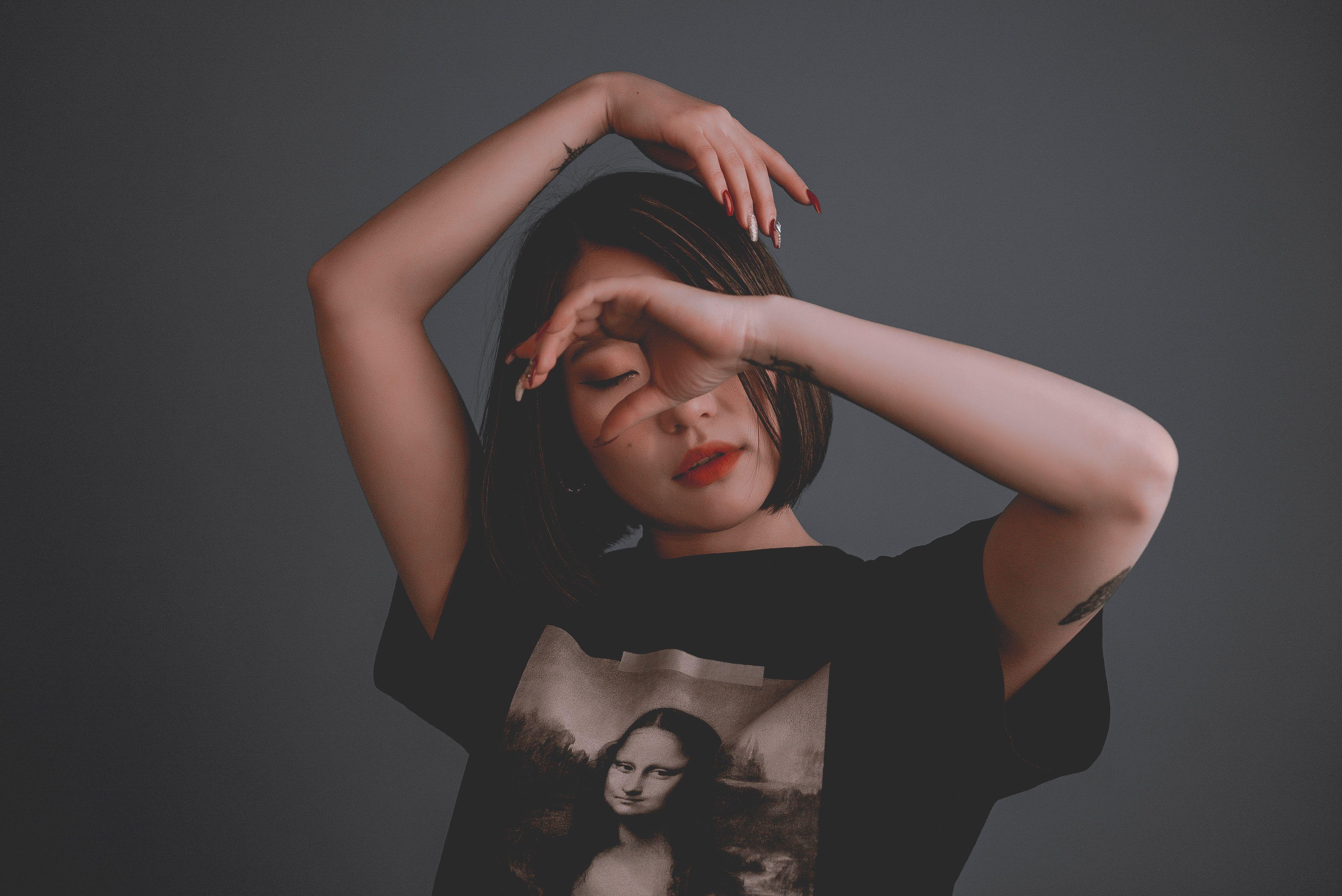 Young reflective ethnic female in stylish t shirt with illustration and red lips standing with closed eyes and raised arms