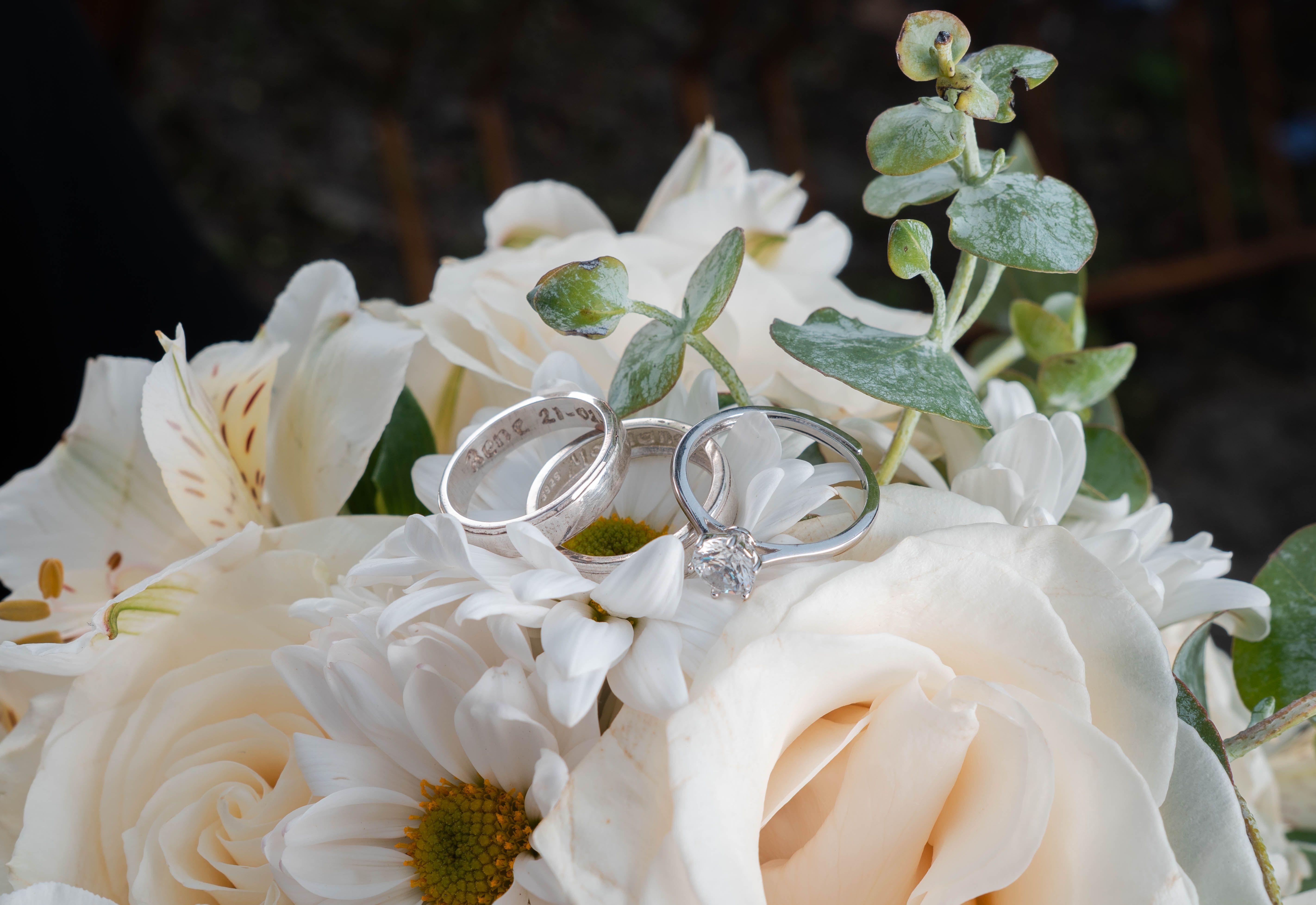 Close-up of wedding rings elegantly placed on a white floral bouquet, symbolizing love and commitment.