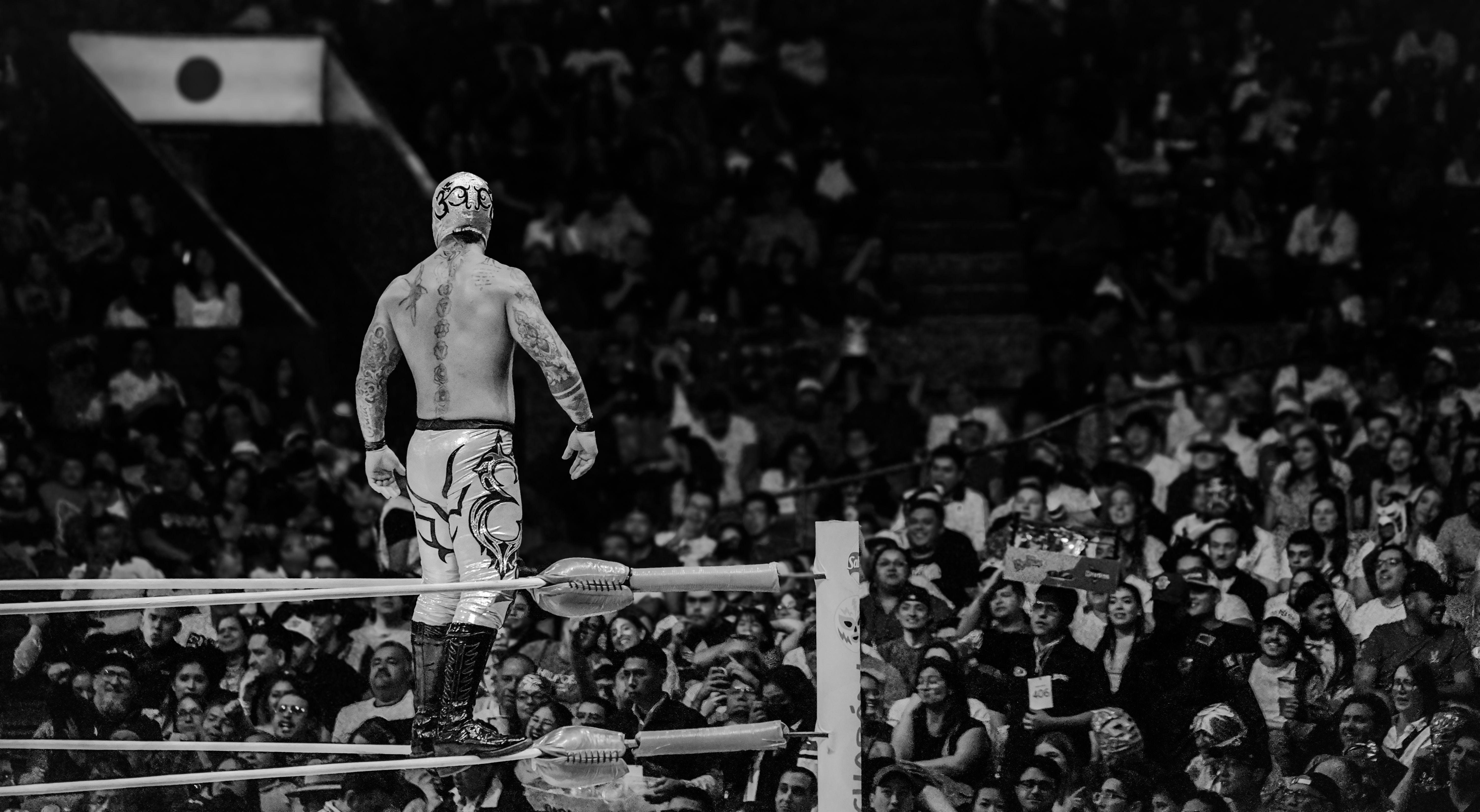 Dramatic black and white shot of a masked wrestler in action before an excited crowd in Ciudad de México.