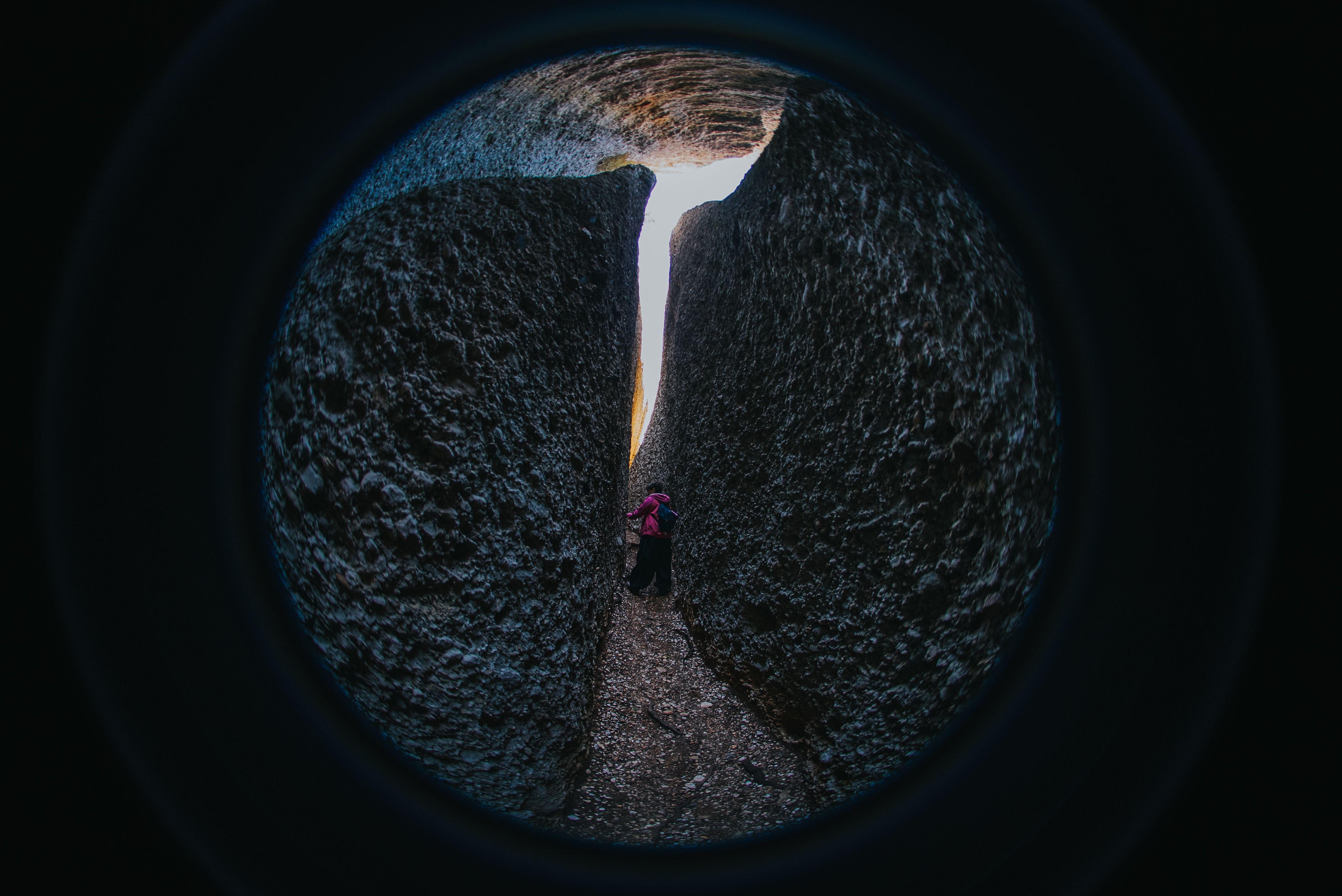 A person navigates a narrow passageway between large rock formations, captured with a fisheye lens.